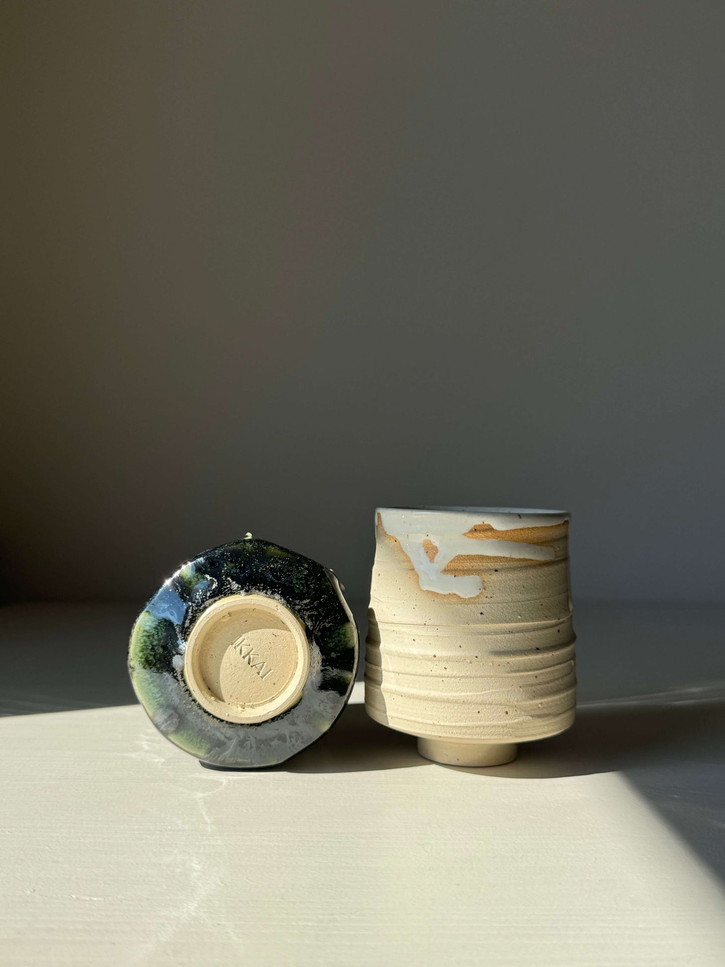 Set of two Yunomi cups from the Yuki & Hinoki series, one in soft tones and one in dark green, made of high-fired stoneware clay.
