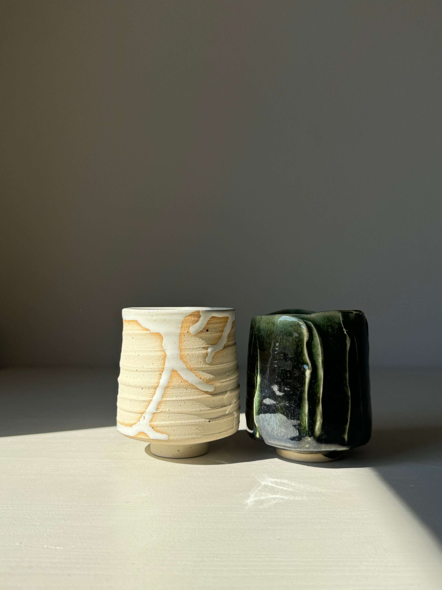Set of Yunomi Cups - Yuki & Hinoki Series, featuring contrasting designs: one in soft white, the other in deep forest green. High-fired stoneware.