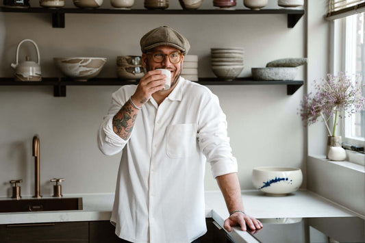 Abel Pepping in his studio, drinking coffee in front of handmade ceramics.