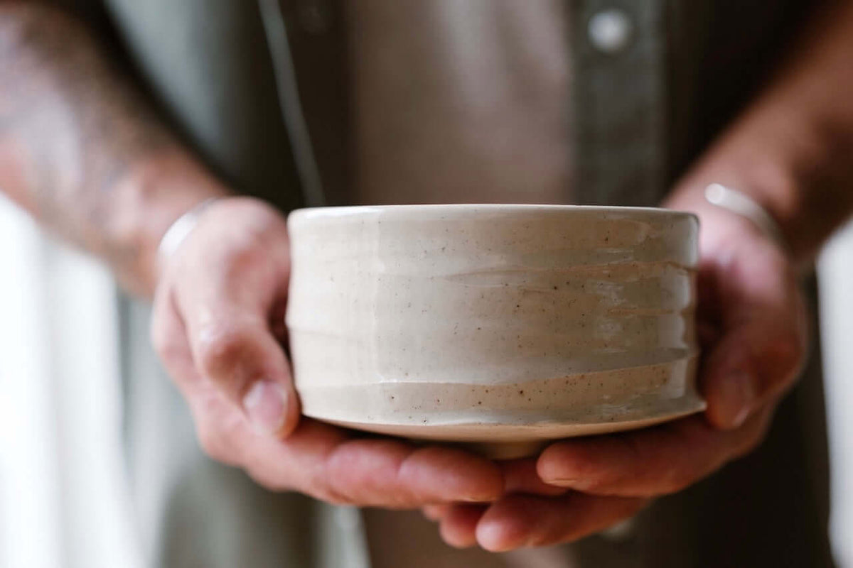 Close-up of hands gently holding a handmade ceramic matcha bowl (chawan) with a natural matte glaze — crafted by IKKAI Ceramics.