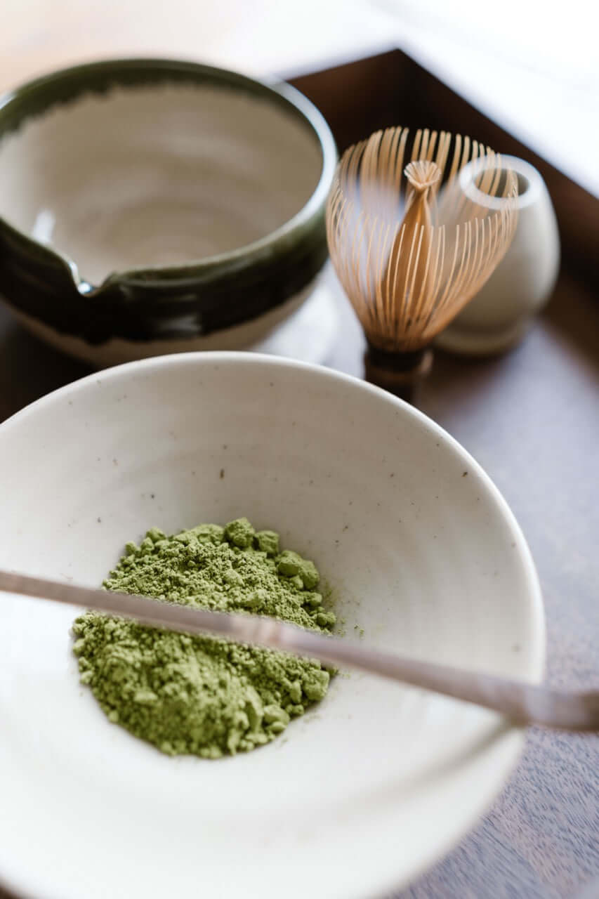 Fresh matcha tea powder in a handcrafted ceramic matcha bowl, with bamboo whisk and scoop in the background — a quiet moment before preparation begins.