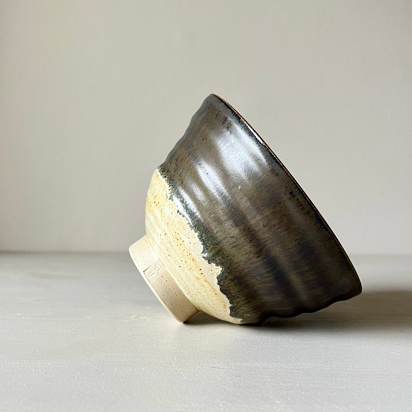 A cream and black ceramic matcha bowl laying on its side on a neutral background