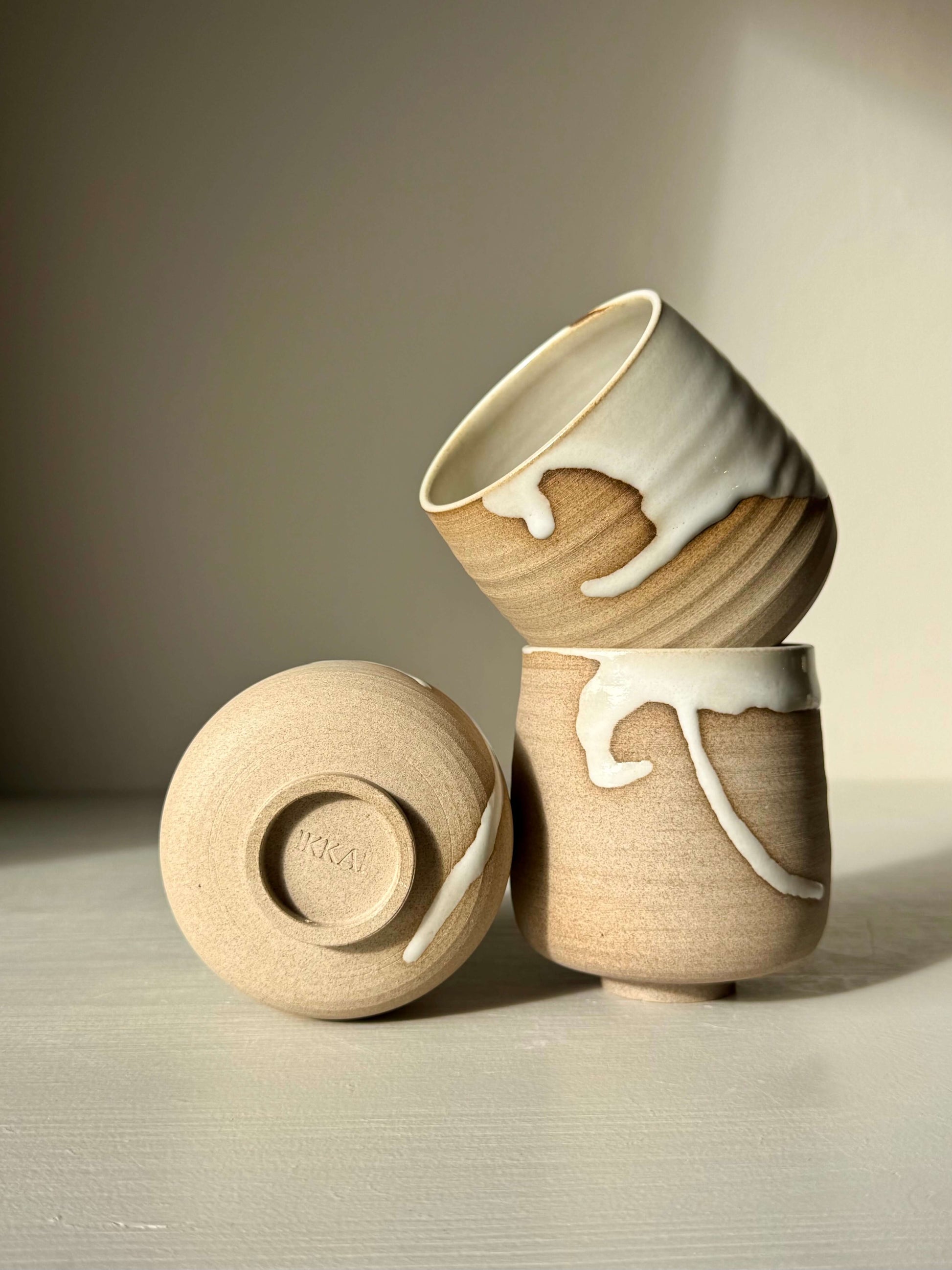Yunomi Cups - Yuki handmade ceramic with white glaze over toffee clay, showing unique drips and raw texture on three stacked cups.