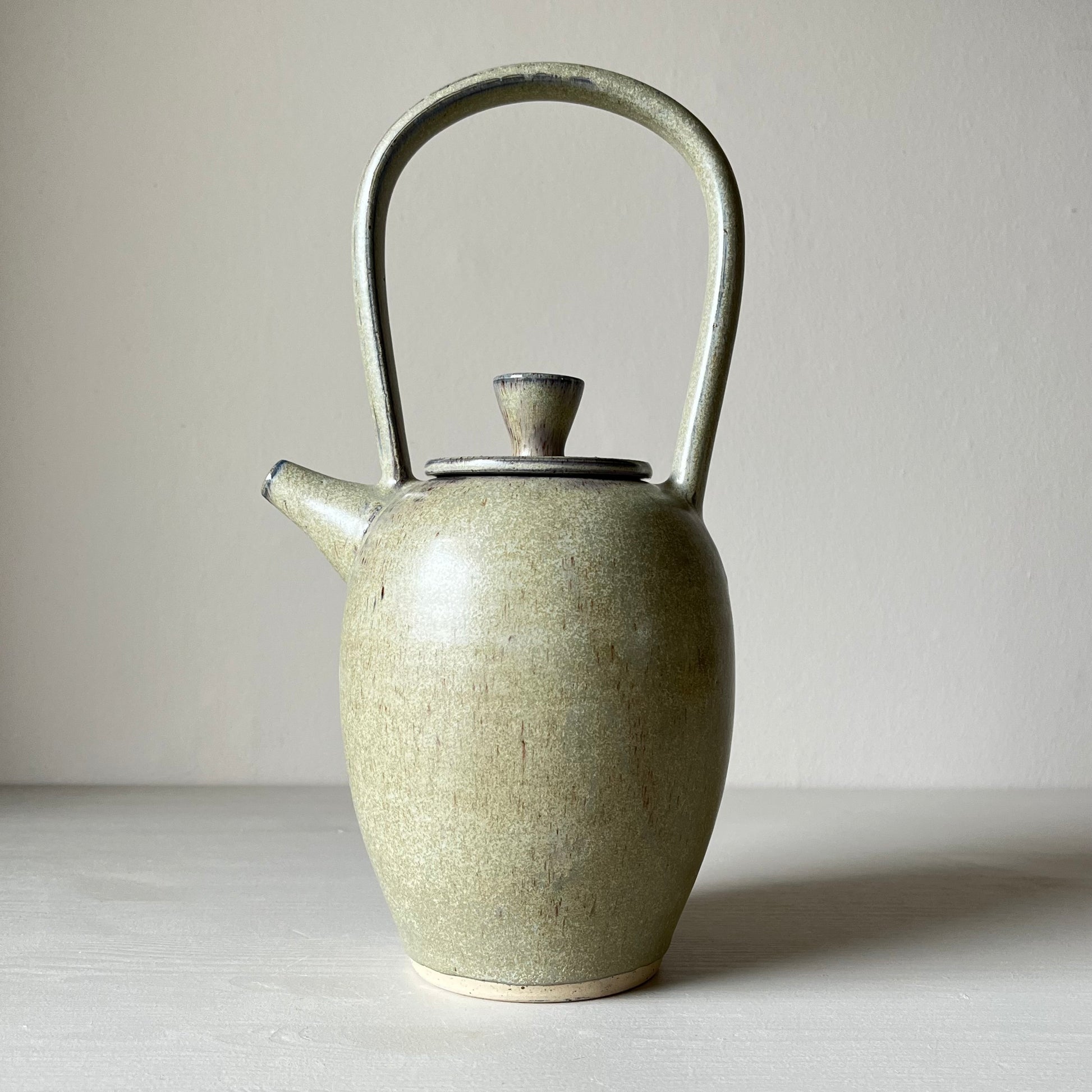 a side view of A blue ceramic teapot on a neutral background