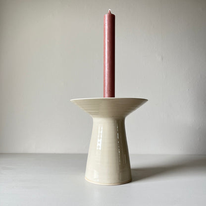 A large cream cermamic candlestick holder holding a pink candlestick