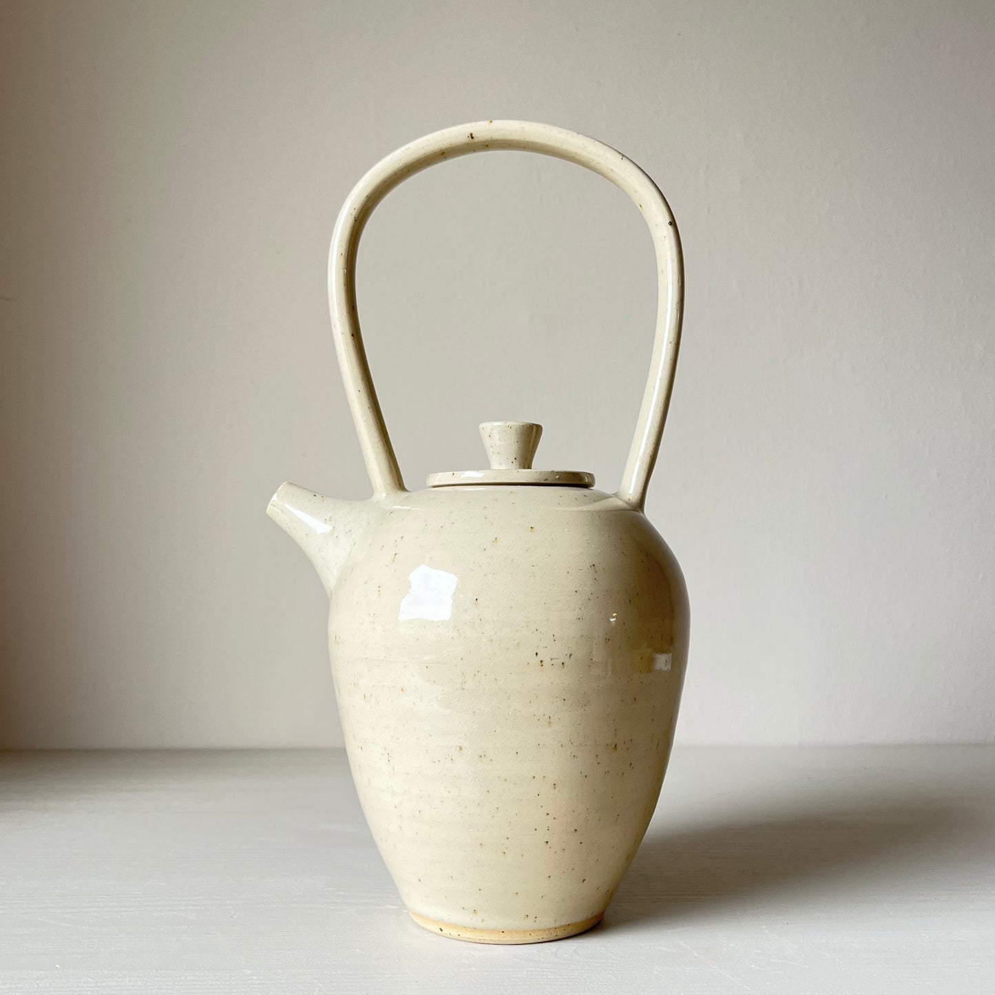 a tall ceramic teapot with a cream coloured glaze on a neutral background