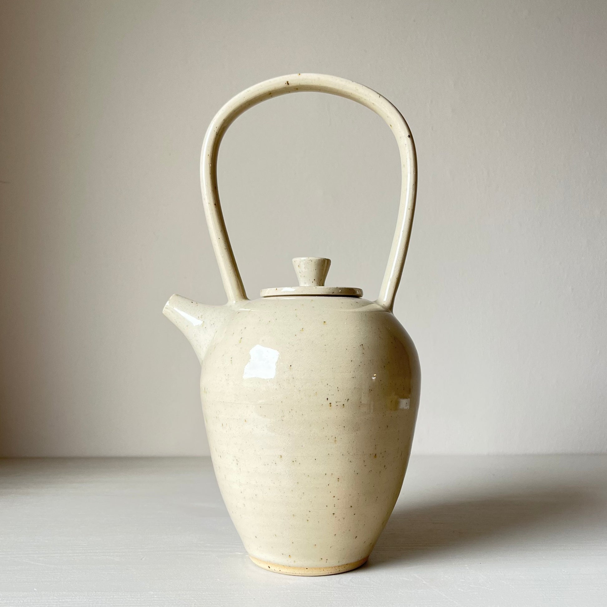 a tall ceramic teapot with a cream coloured glaze on a neutral background