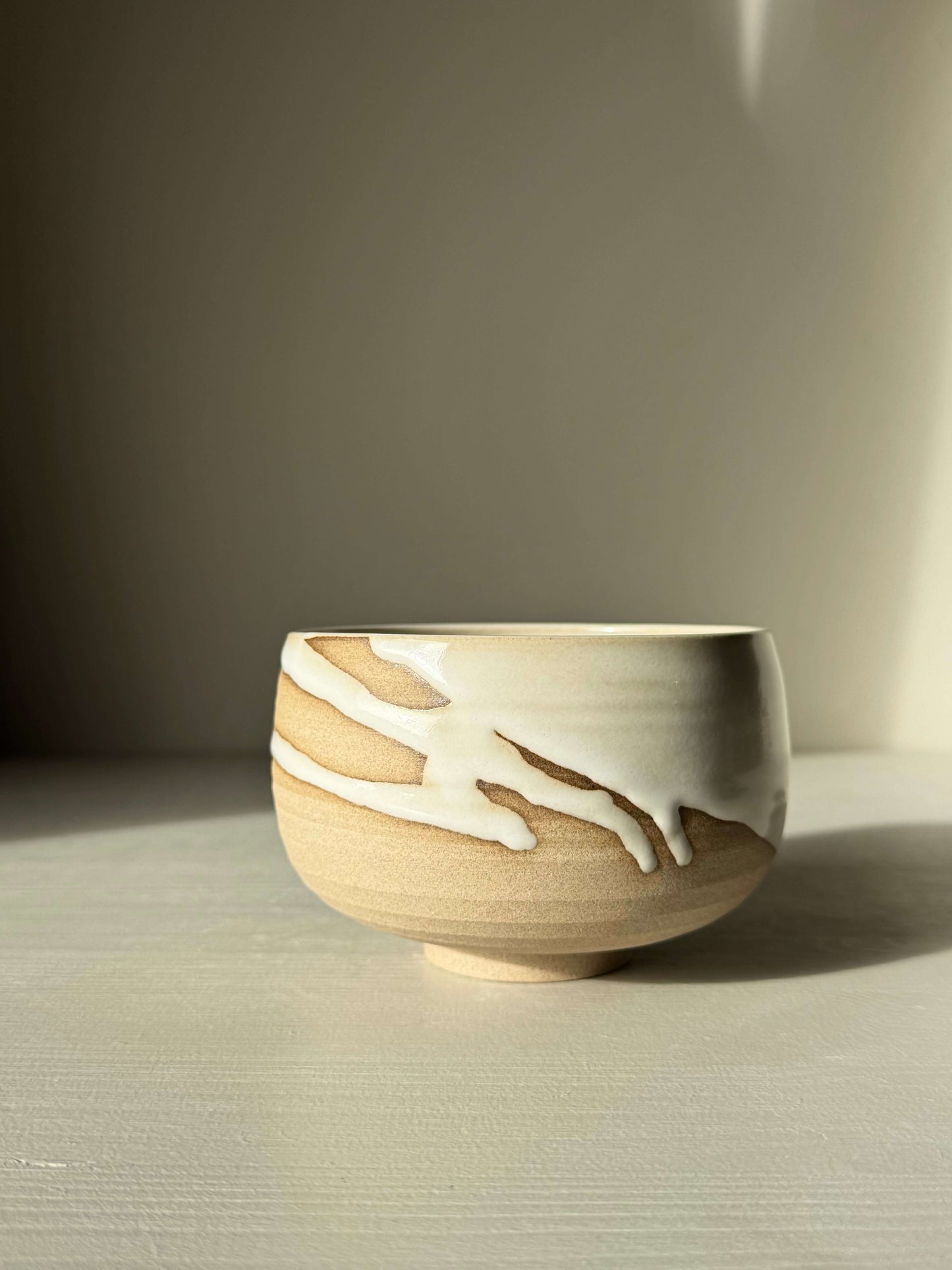 Handmade ceramic Matcha Bowl – Yuki #03 with toffee clay and glossy white glaze, showcasing unique drip patterns under natural light.