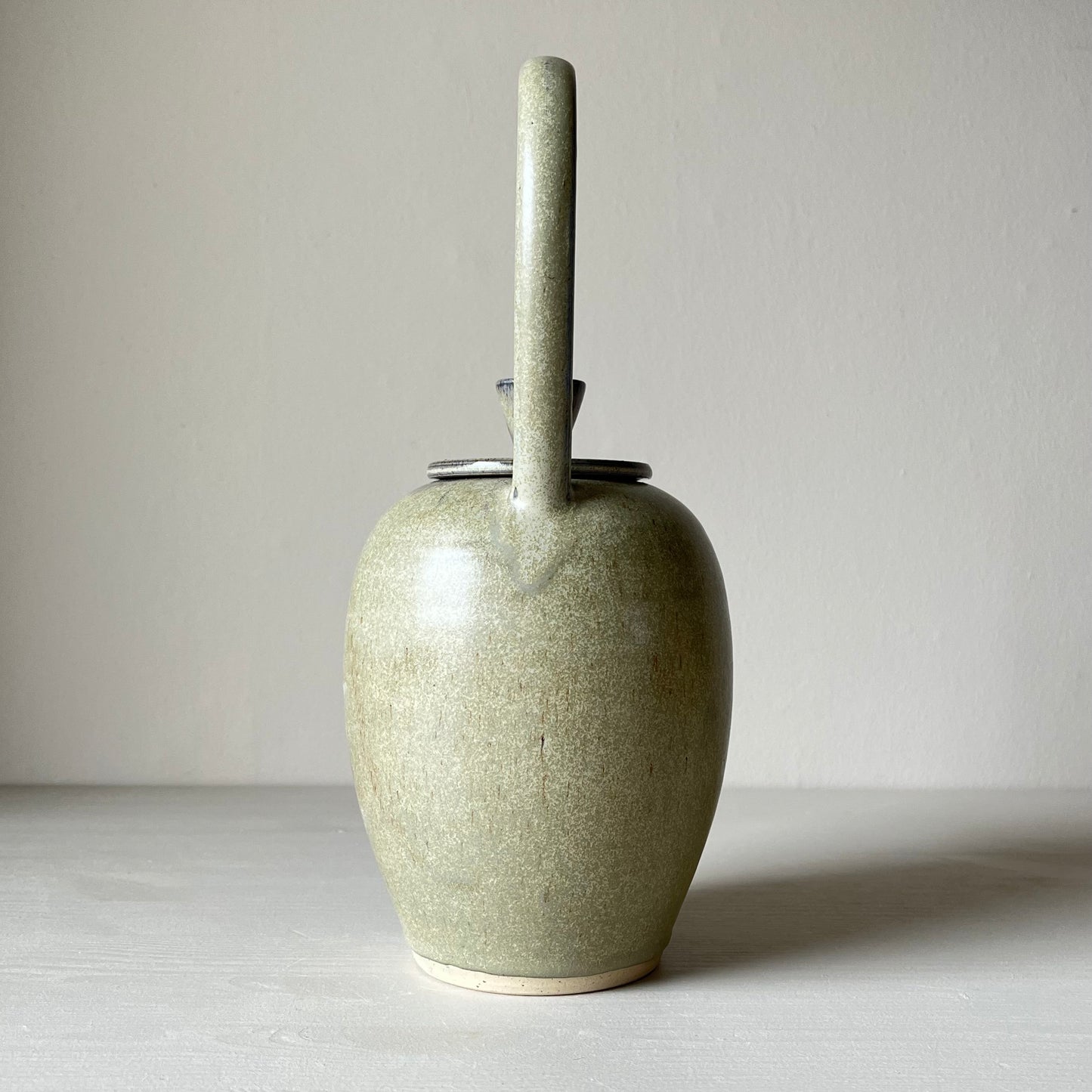 back view of a blue ceramic teapot on a neutral background