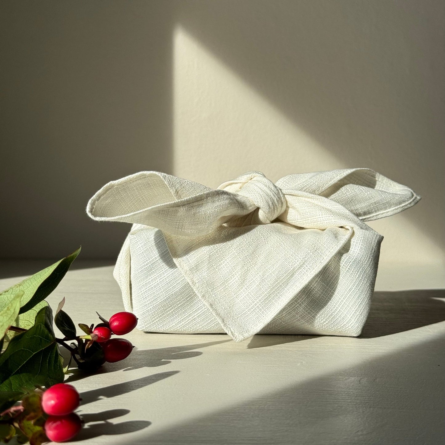 Small present wrapped in a cream furoshiki on a neutral background