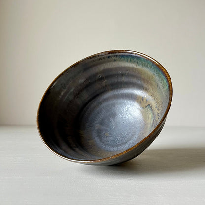 A black ceramic matcha bowl laying on its side on a neutral background