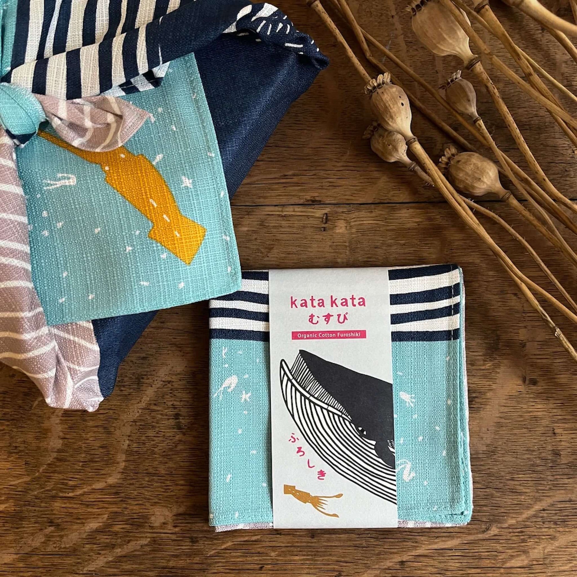 Small Furoshiki kata kata musubi organic cotton Blue Whale with patterned fabric and a label on a wooden surface.