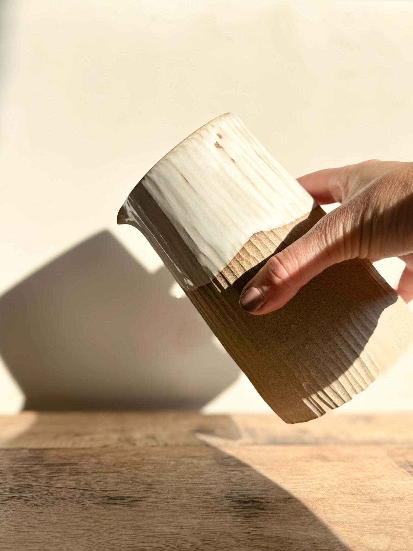 Hand holding medium Yuki Series vase with sculptural design, glossy white glaze, unglazed textured base, perfect as vase or pitcher.