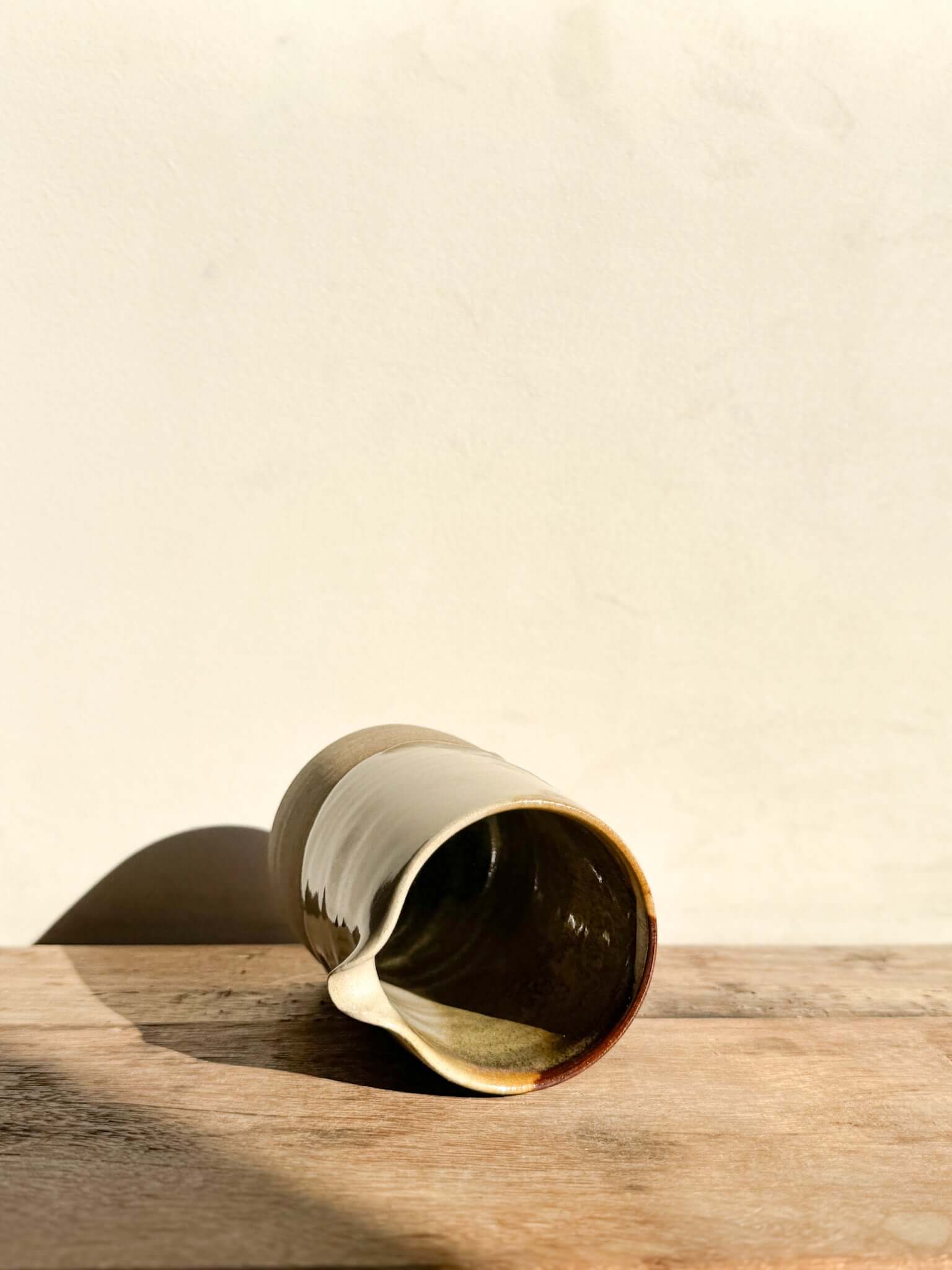 Small Vase / Jug from Inyo Series #02 with flowing glaze on wooden surface, showcasing textured and smooth clay contrast.