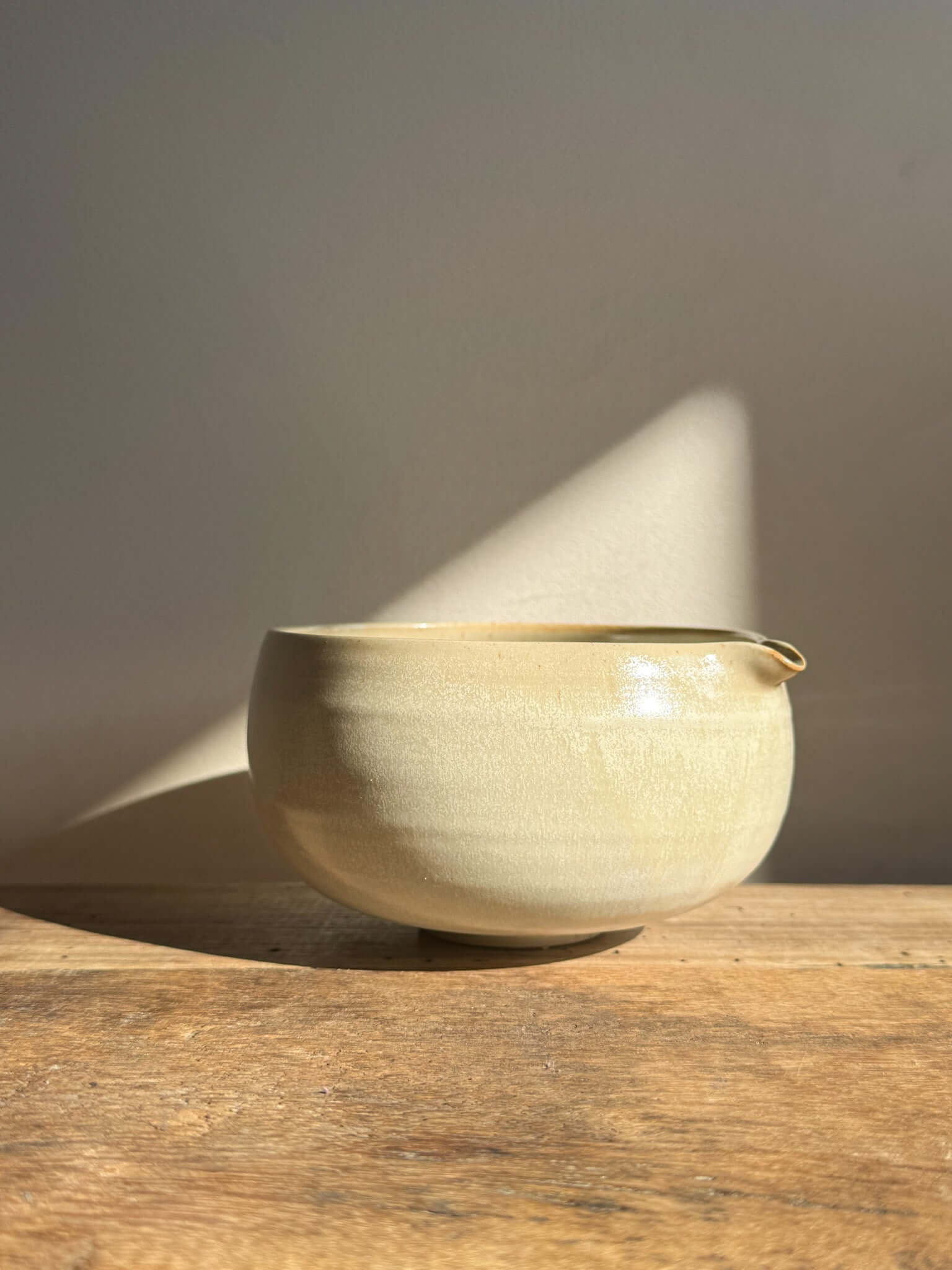 Katakuchi Matcha Bowl with Spout in Moonstone glaze on wooden surface, highlighting its soft, rounded design and smooth pouring spout.