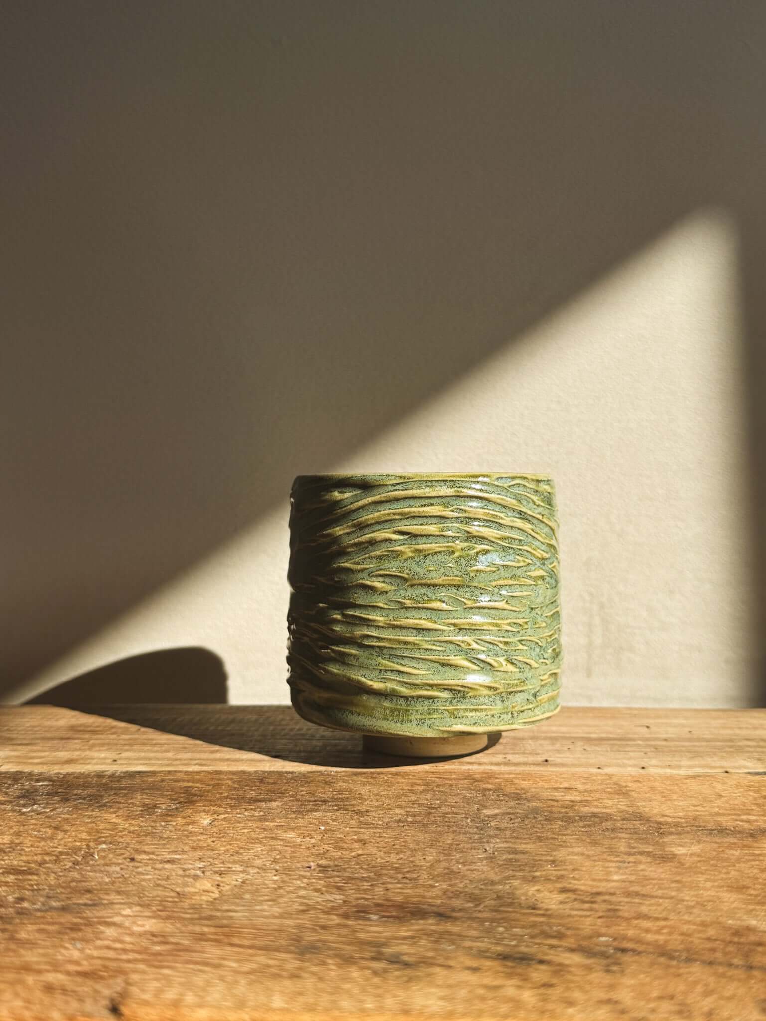 Wasabi Green Yunomi Cup with textured surface and subtle shine, displayed on wooden table with soft lighting.
