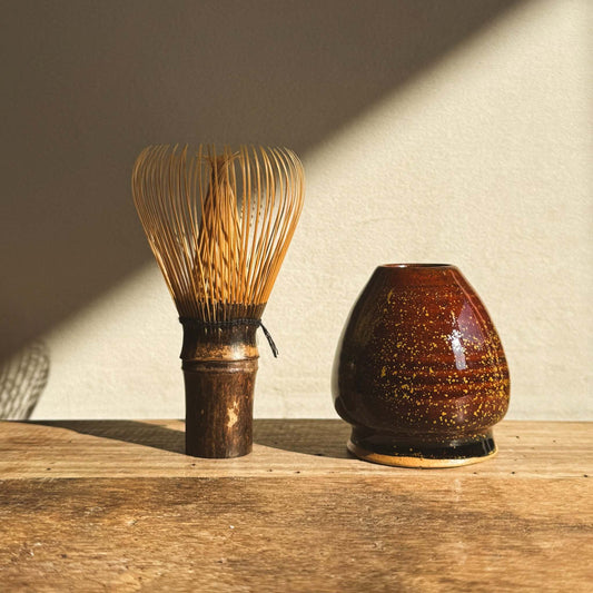 Amber glazed Matcha whisk holder with bamboo whisk on wooden surface, enhancing tea setup aesthetics.