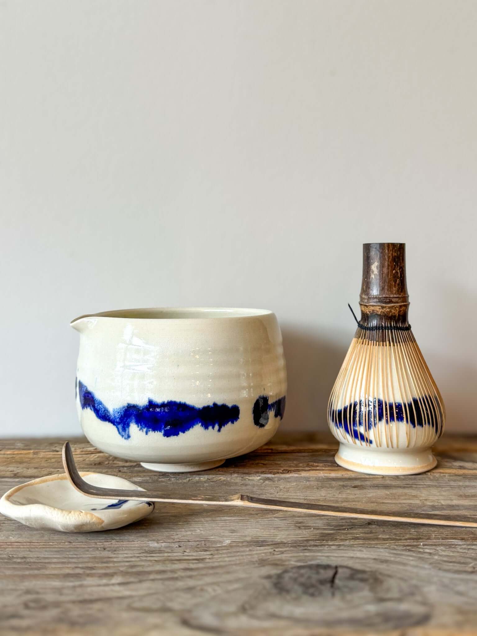 Katakuchi Matcha Bowl with Spout from Gosu Series, featuring cobalt blue glaze patterns, whisk, and spoon on a rustic surface.