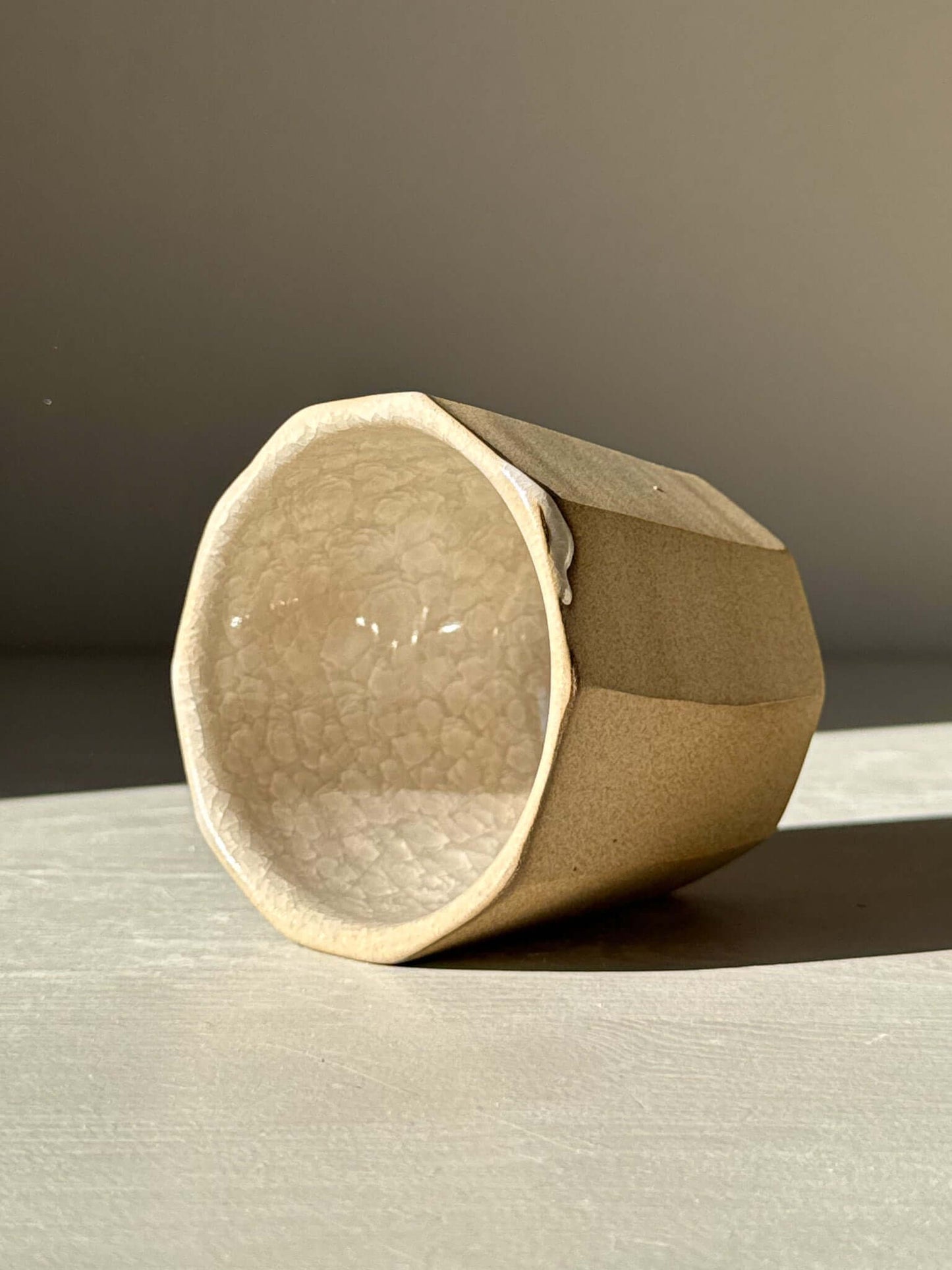 Faceted yunomi cup - Crackle Glaze with geometric design and glossy interior on display table.