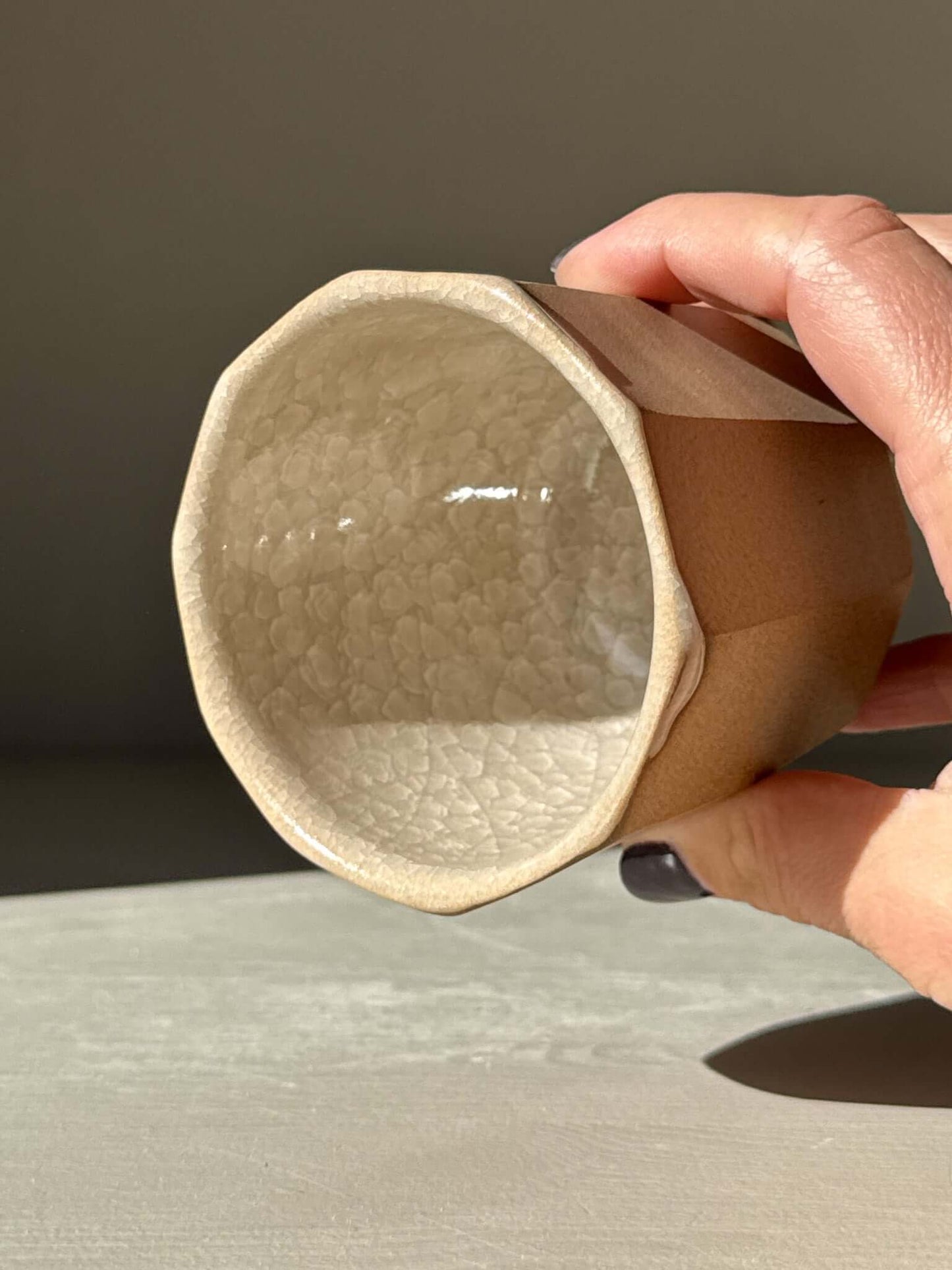 Hand holding faceted yunomi cup - Crackle Glaze, displaying geometric design with glossy crackle glaze inside and natural clay exterior.