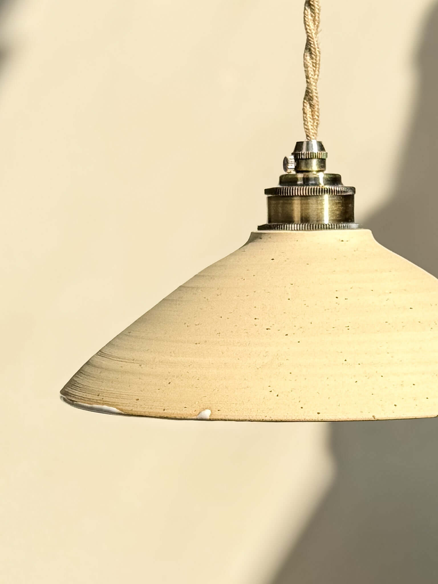 Ceramic Lamp Shade – Half Glossy White Glaze #02 hanging against a beige wall, showcasing its natural clay texture and glossy white interior.