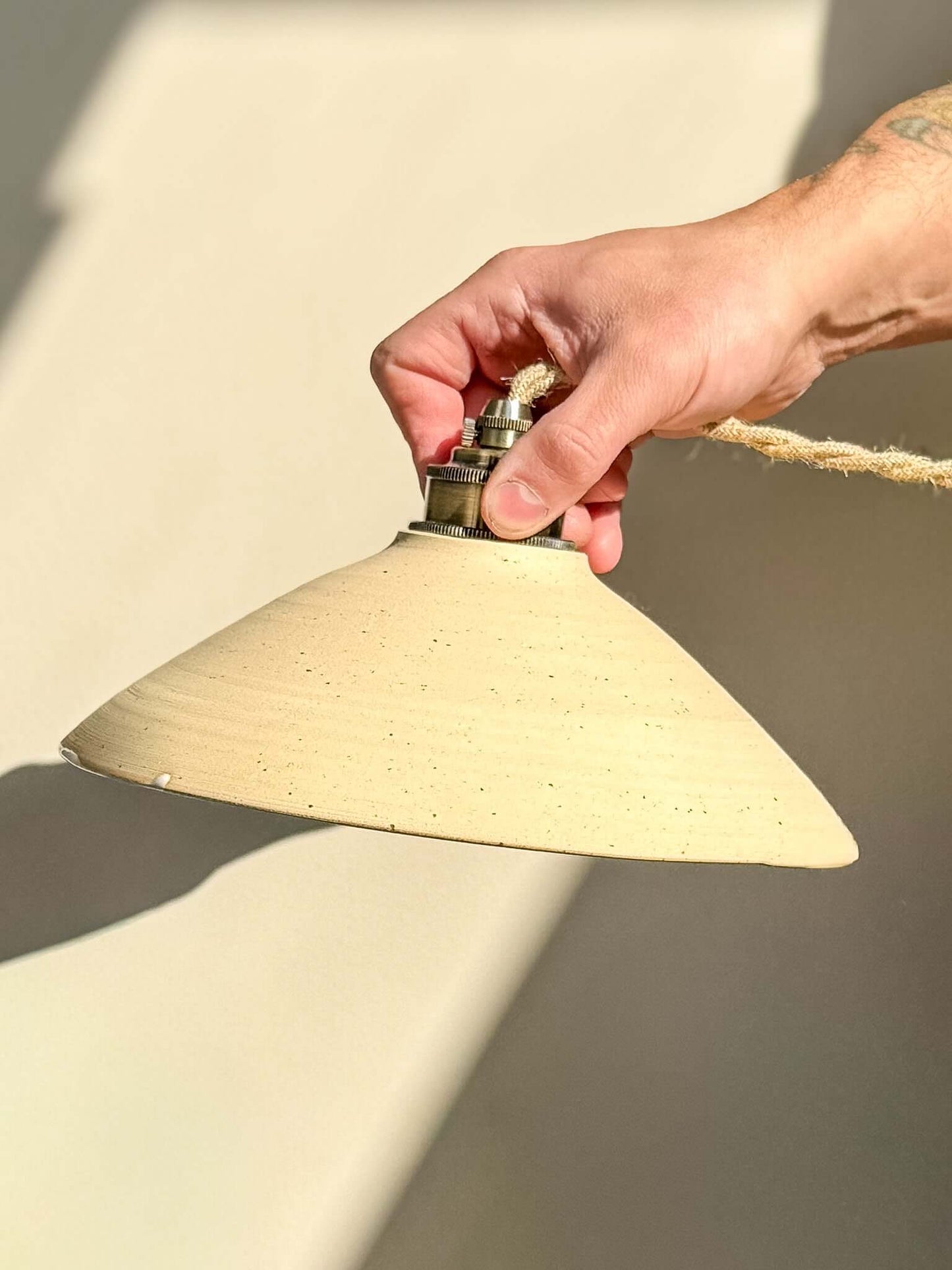 Close-up of Ceramic Lamp Shade – Half Glossy White Glaze #02 with raw exterior and glossy white interior, held by a hand with sunlight reflection.