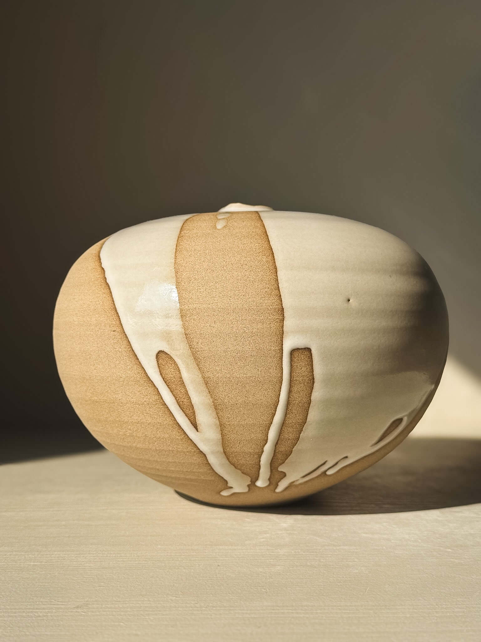 Orb Vase – #19 with unique glaze patterns and soft spherical design, showcasing its sculptural presence in a warm setting.