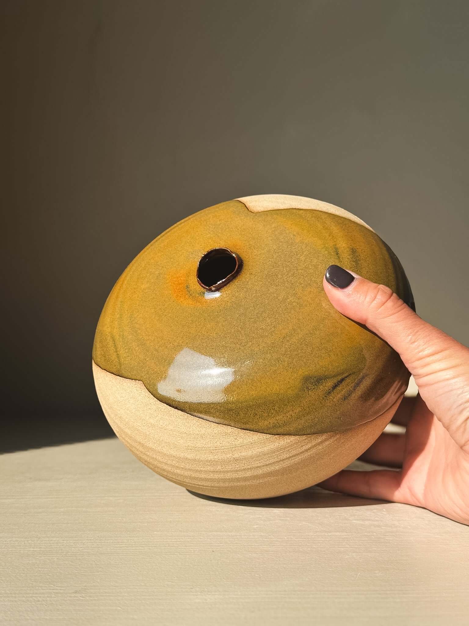Hand holding Orb Vase – #18 showcasing unique glaze patterns and rounded sculptural form.