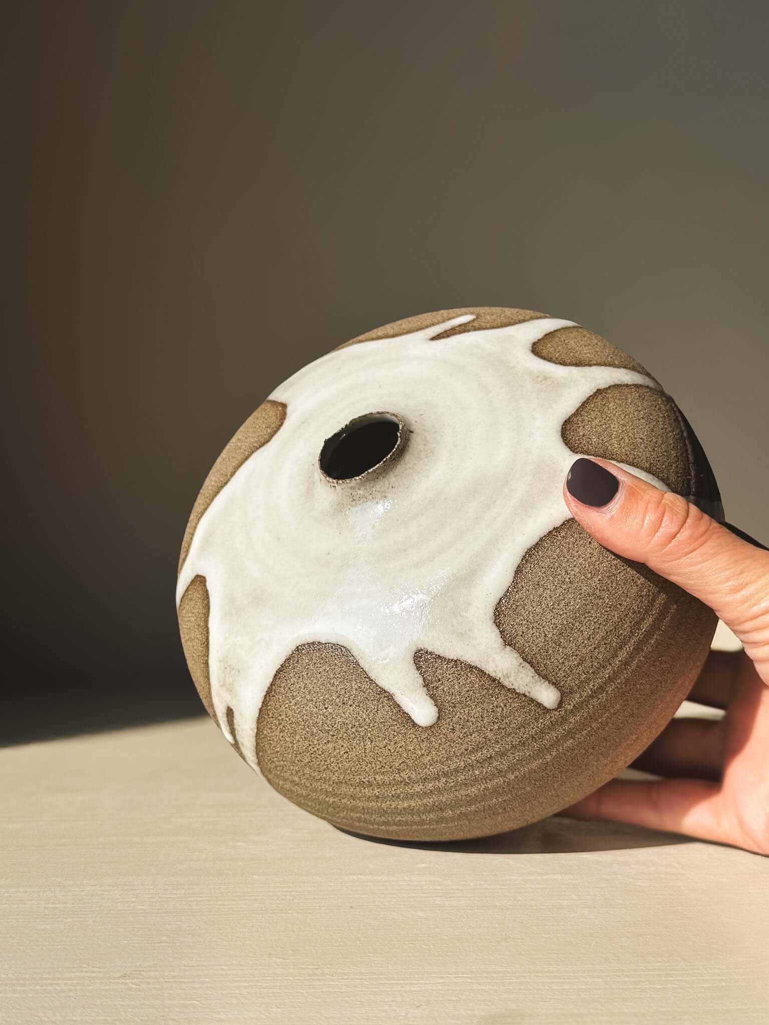 Hand holding Orb Vase – #17, showcasing unique glaze drips and spherical design against neutral background.