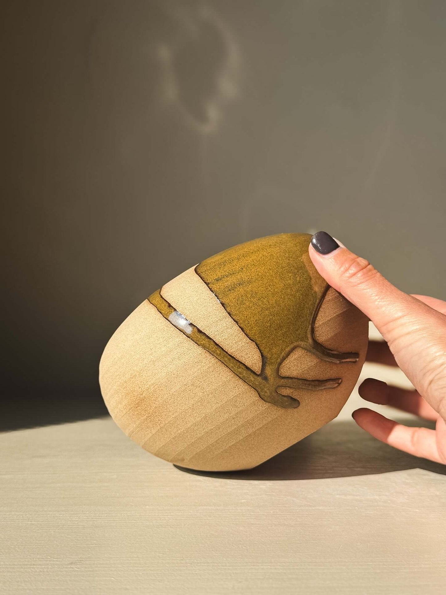 Hand holding Orb Vase – #15 with unique glaze pattern, showcasing its calm, rounded design and sculptural presence.