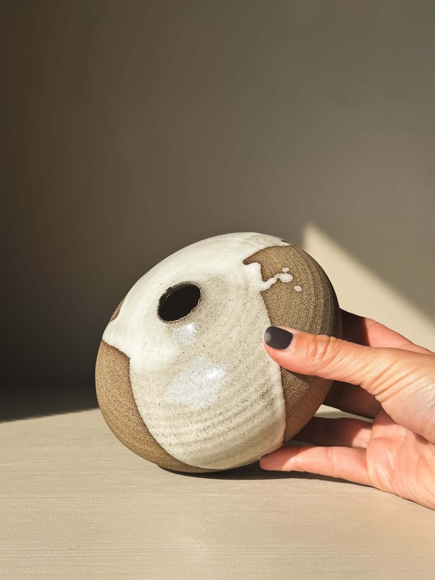 Hand holding Orb Vase – #13 with unique glaze patterns and round shape.