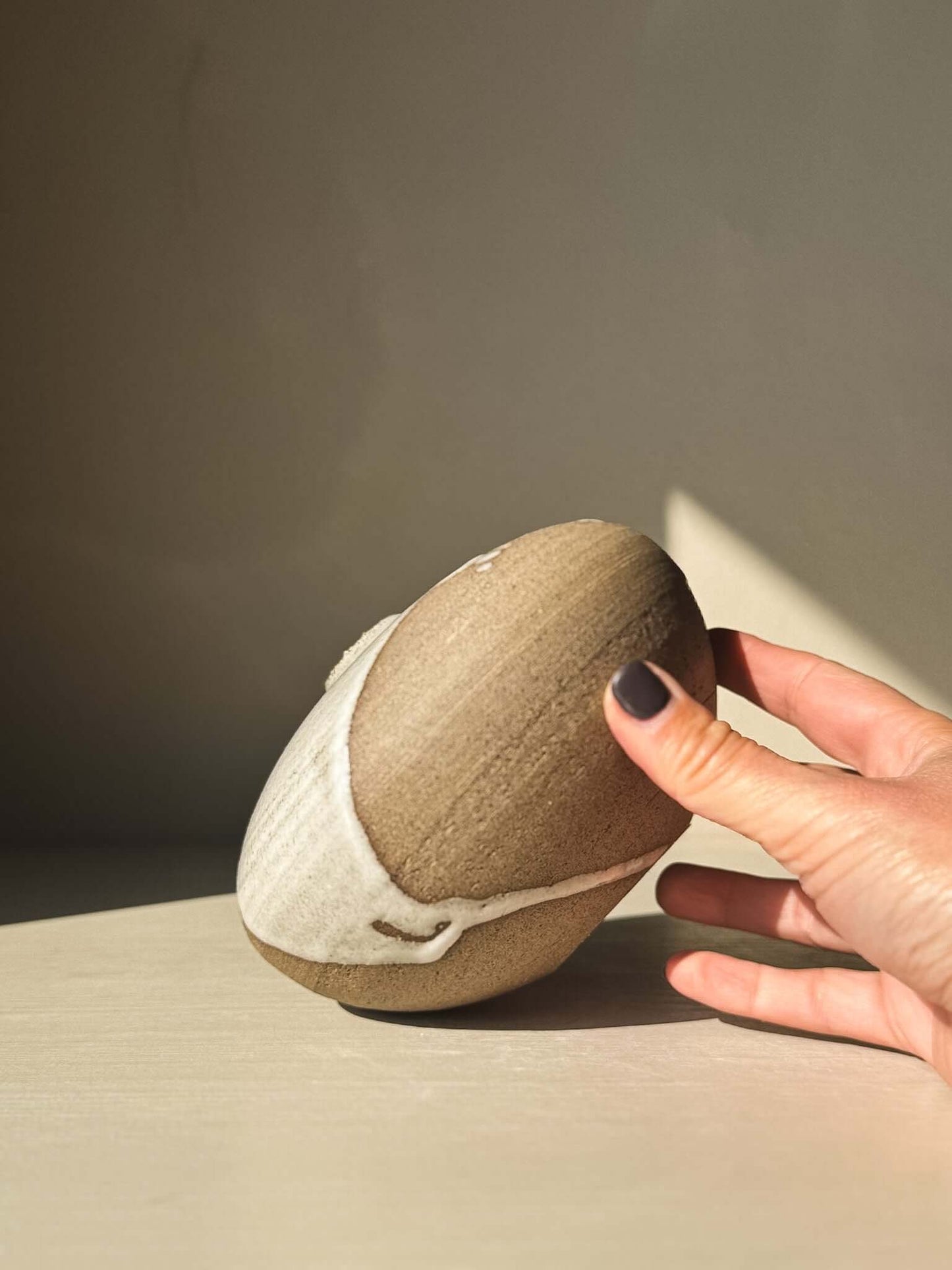 Hand holding Orb Vase – #13 with unique glaze and organic patterns on a soft, rounded form, showcasing artisanal craftsmanship.