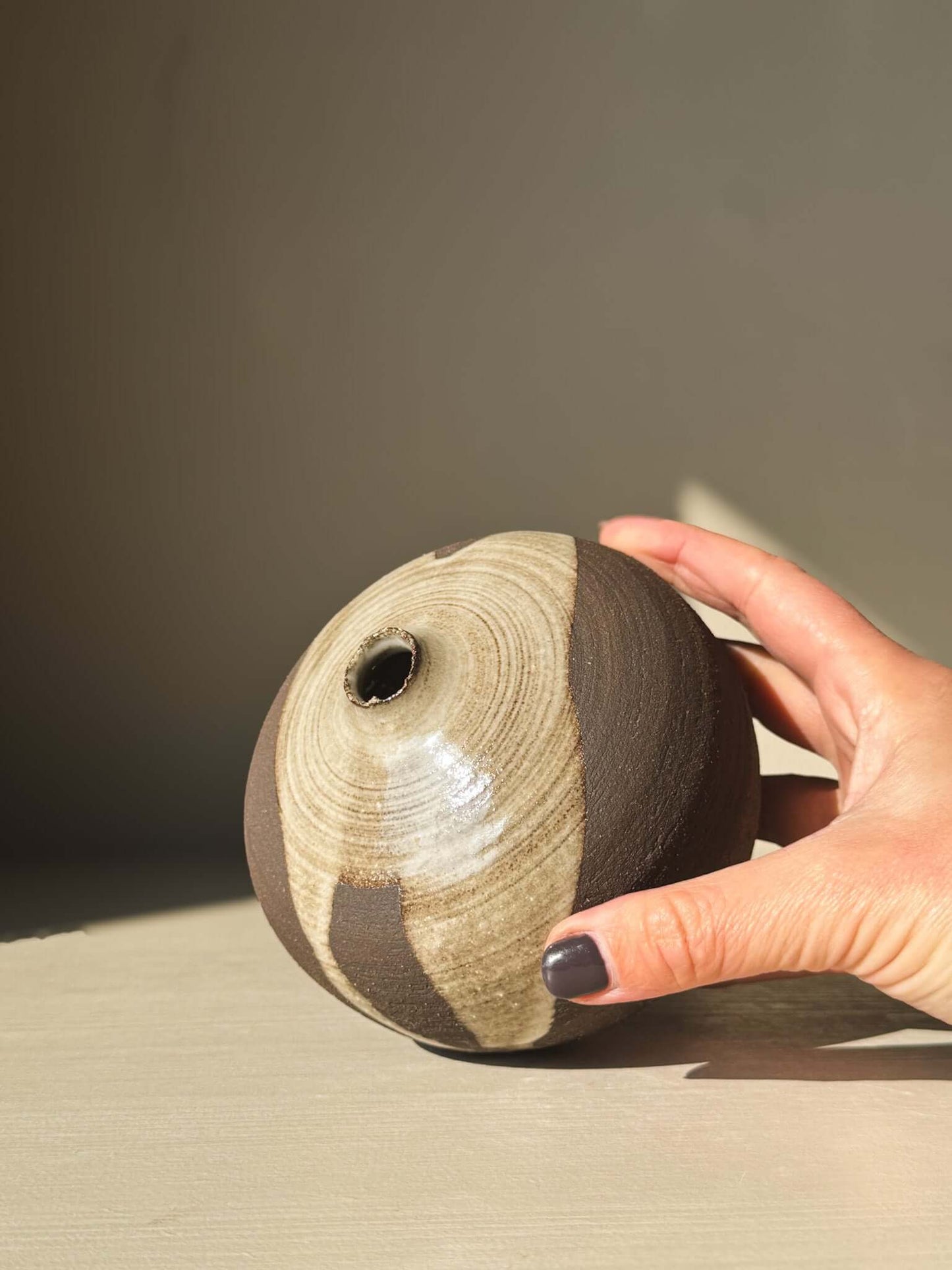 Hand holding Orb Vase – #11, showcasing unique organic glaze patterns and rounded shape from the new collection of sculptural vases.