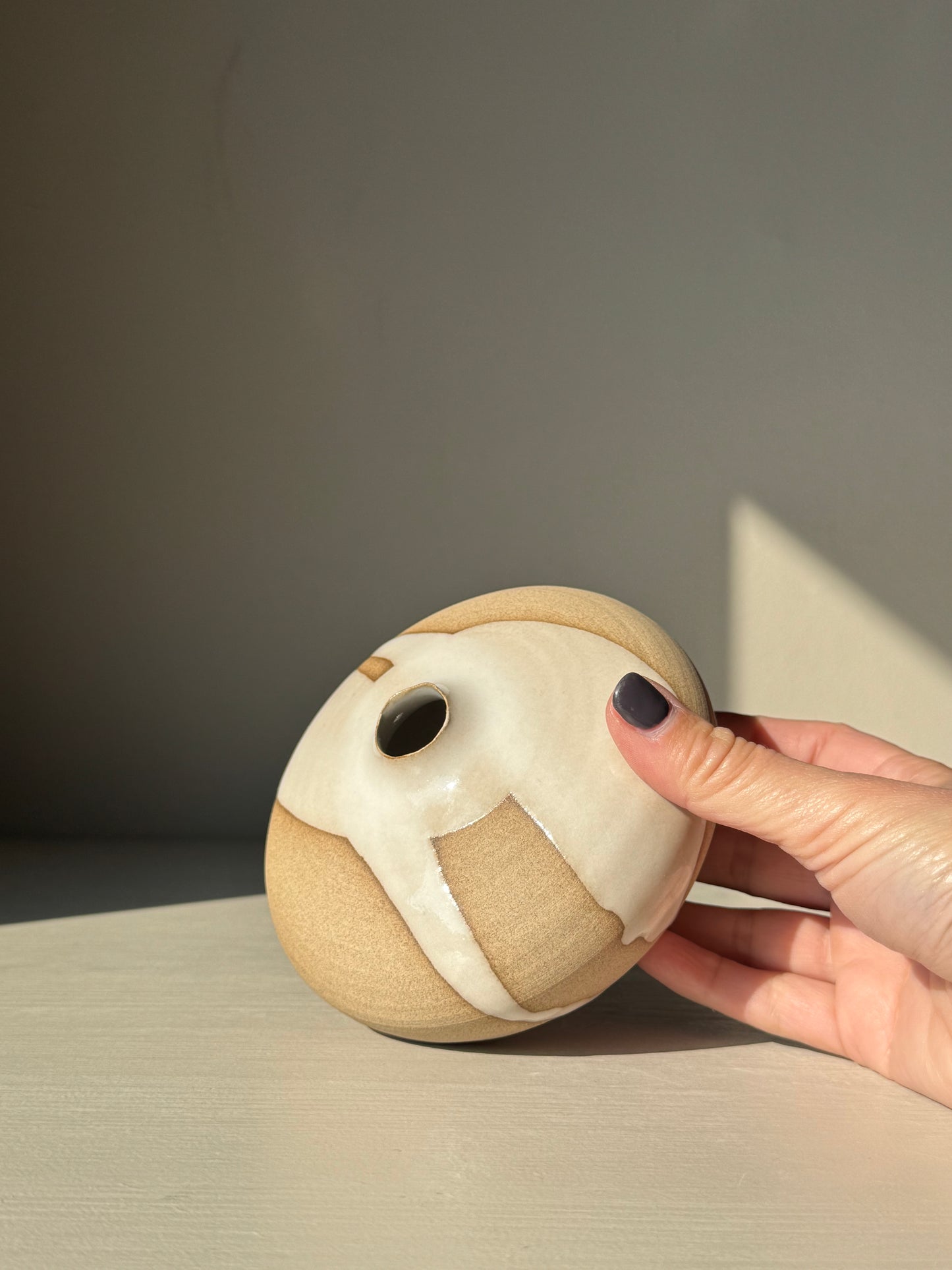 Person holding a small ceramic ball with a face design against a neutral background