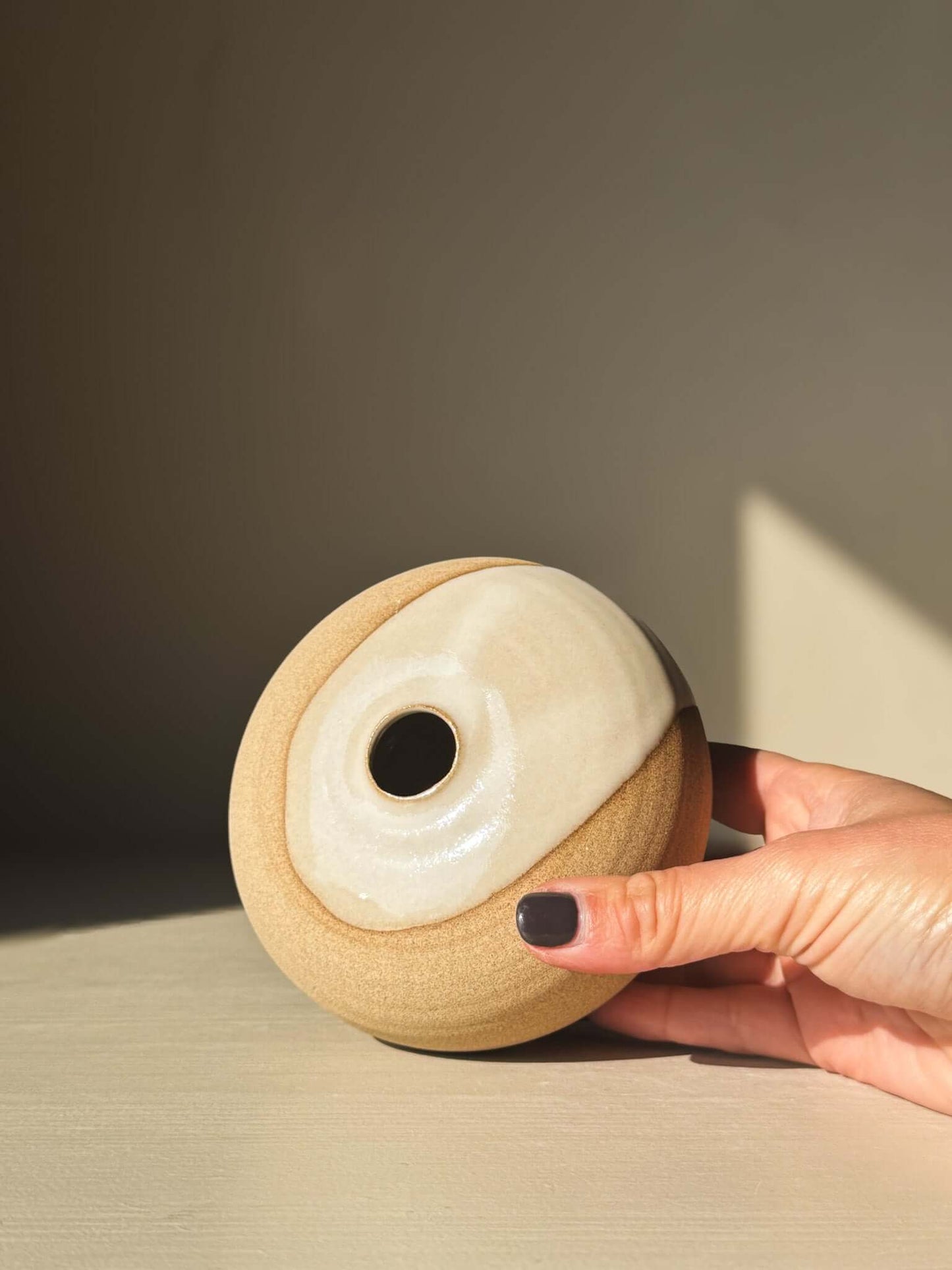 Hand holding Orb Vase – #06 with natural glaze and organic patterns, showcasing its calm, sculptural presence.