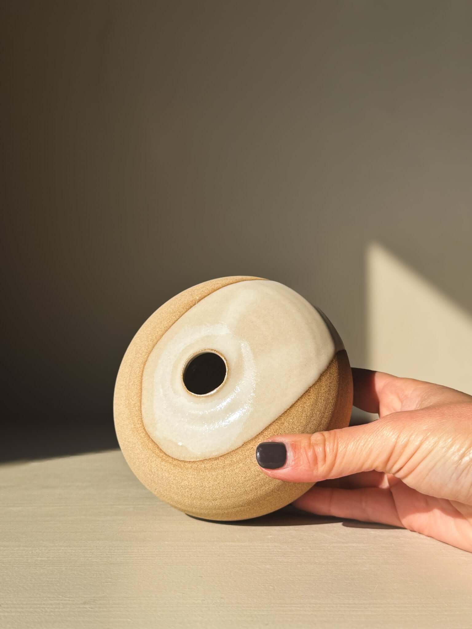 Hand holding Orb Vase – #06 with natural glaze and organic patterns, showcasing its calm, sculptural presence.