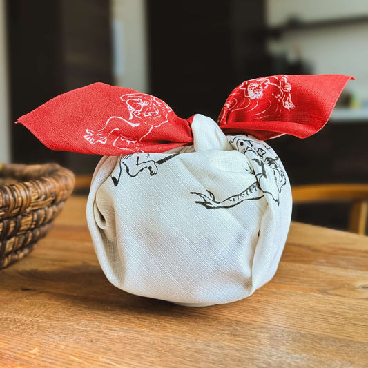 Medium Furoshiki Round Window Red with playful animal designs on a white fabric, tied with a vibrant red scarf.