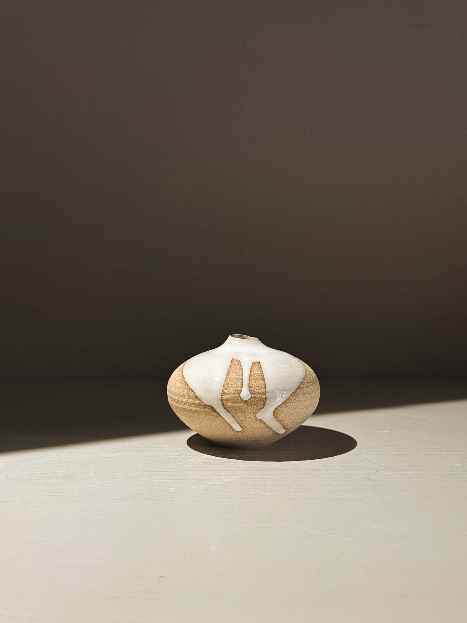 Orb Vase – Yuki #09 in soft spherical form with unique glaze patterns casting shadows on a surface.