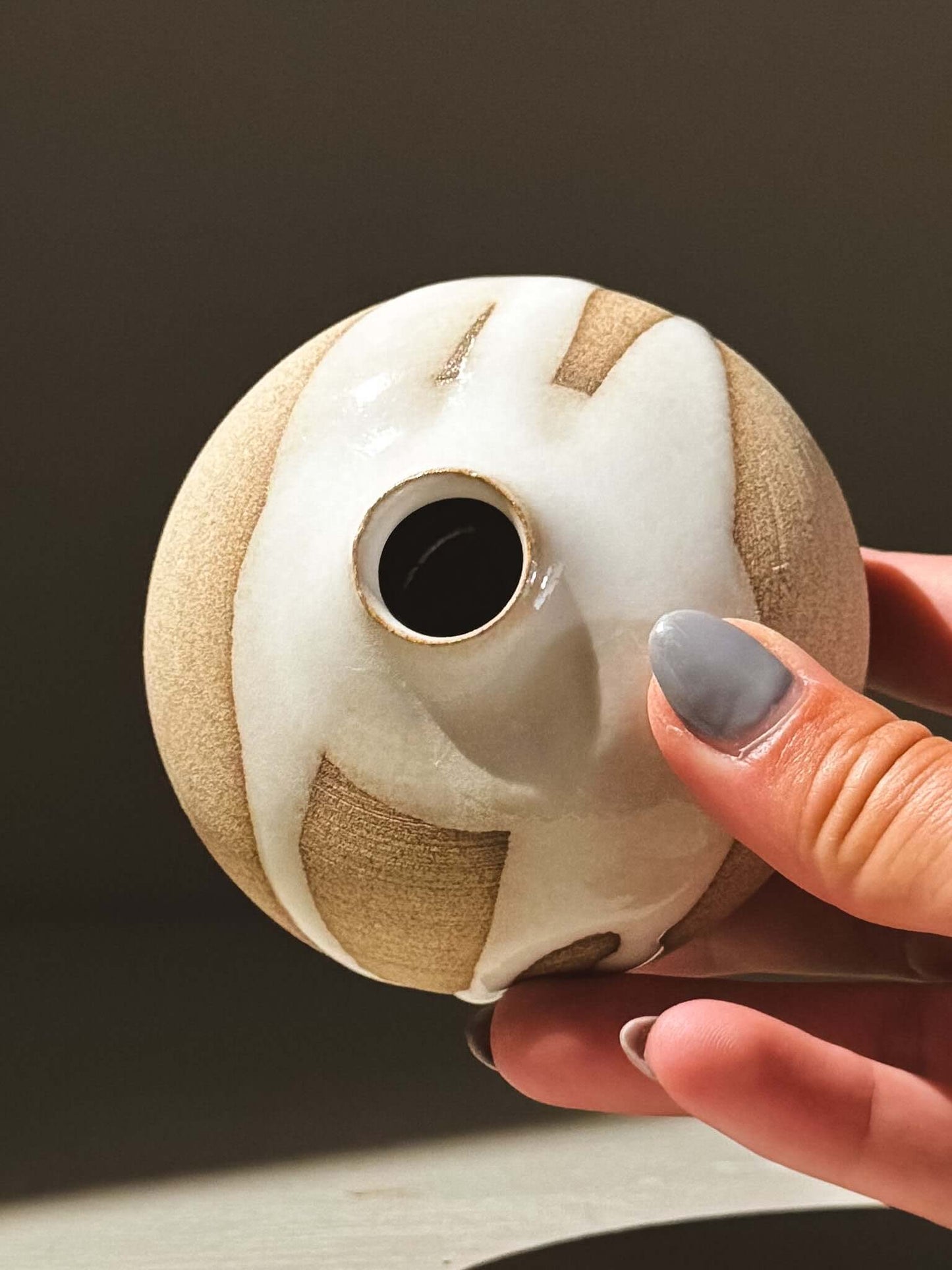 Hand holding an Orb Vase – Yuki #11 showcasing its unique glaze patterns and soft spherical shape.