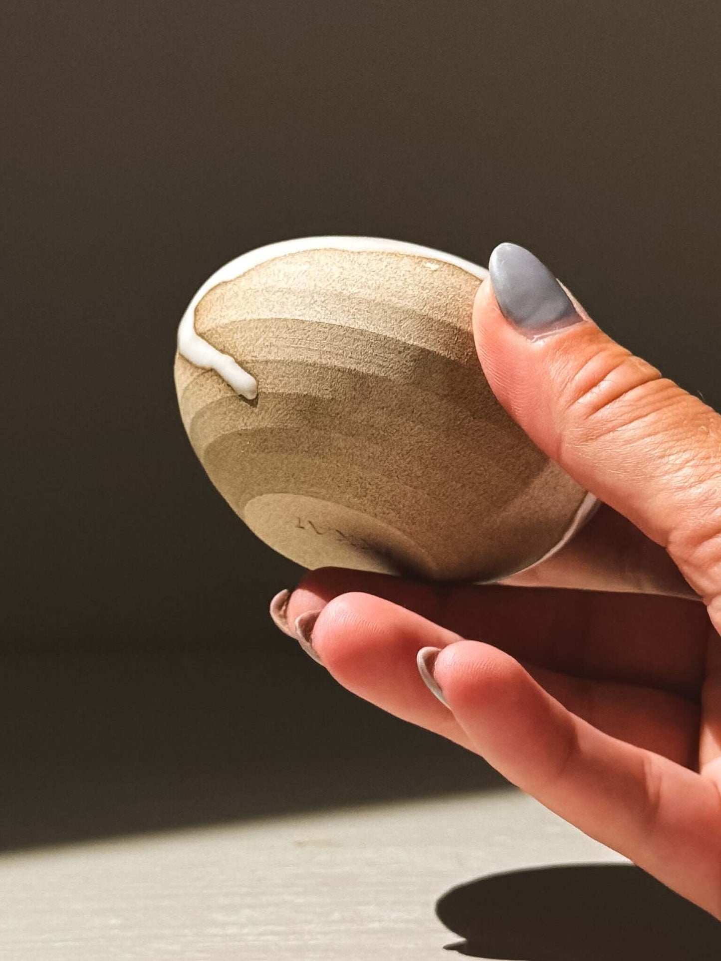 Hand holding an Orb Vase – Yuki #12, showcasing its unique glaze patterns and soft spherical form.