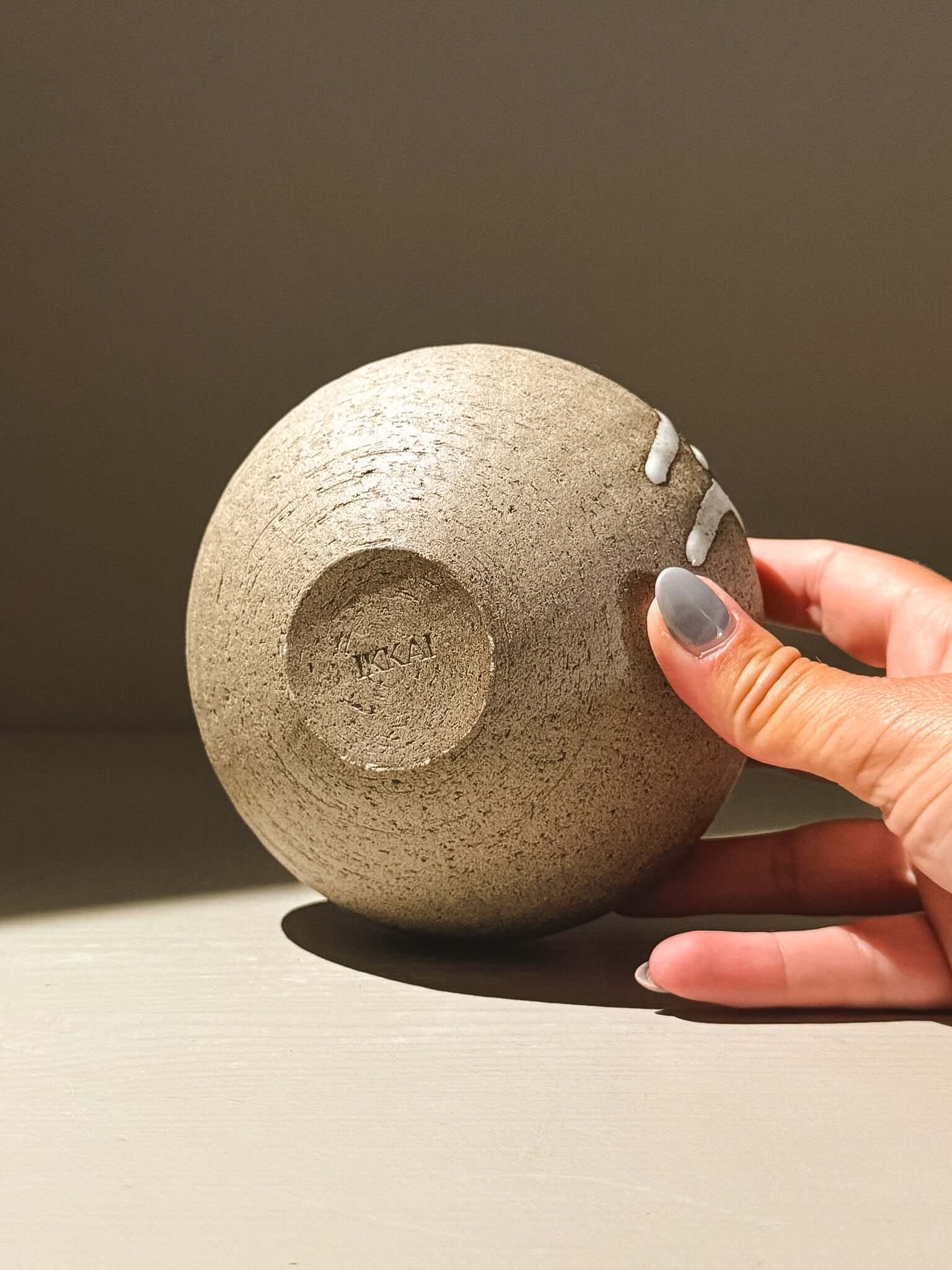 Hand holding the Orb Vase – Yuki Ash #04 with unique texture and glaze pattern in a soft light.