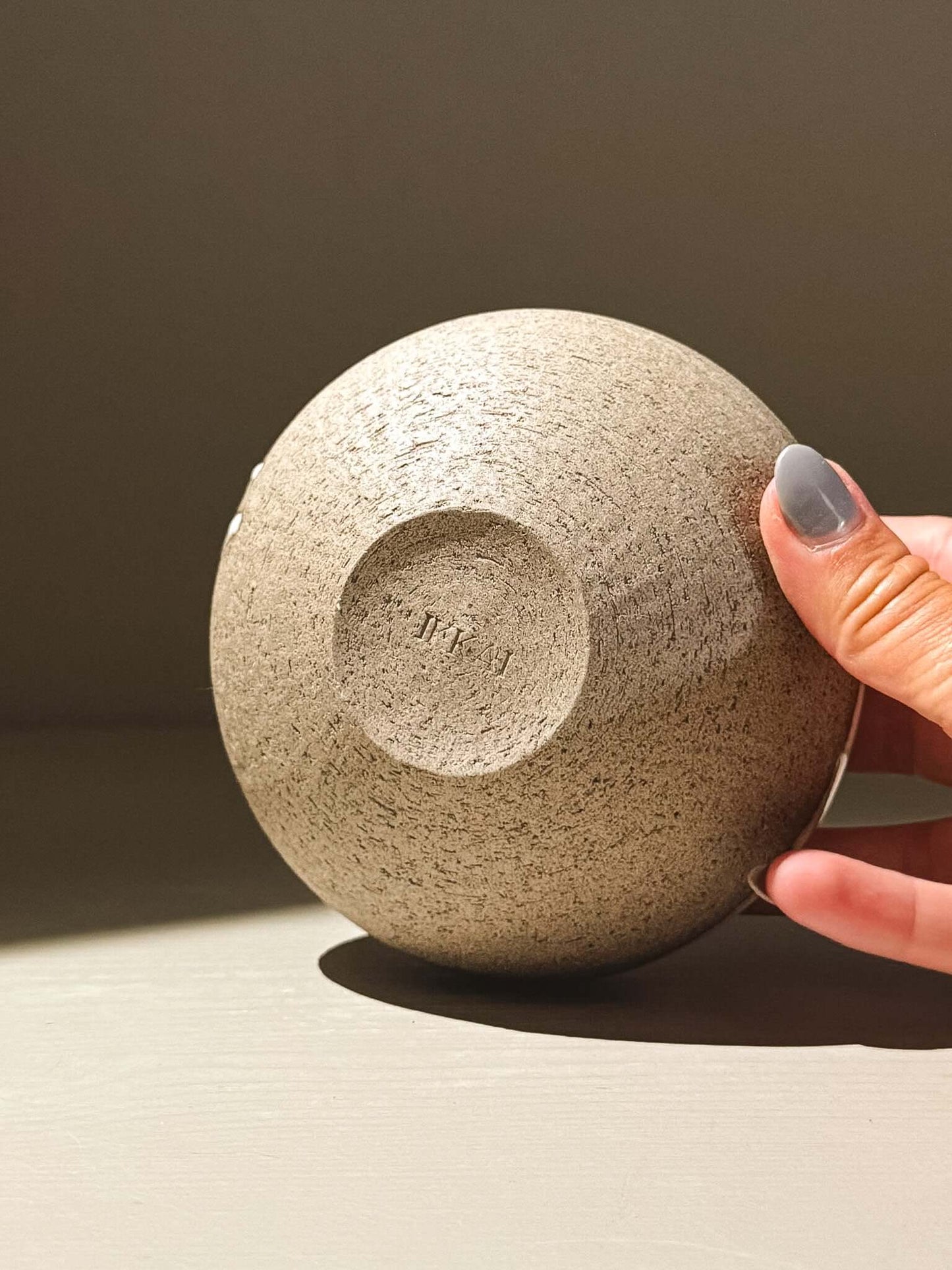 Hand holding the base of the Orb Vase – Yuki Ash #08, showcasing its unique texture and rounded design. Japanese handmade ceramic orb vase.