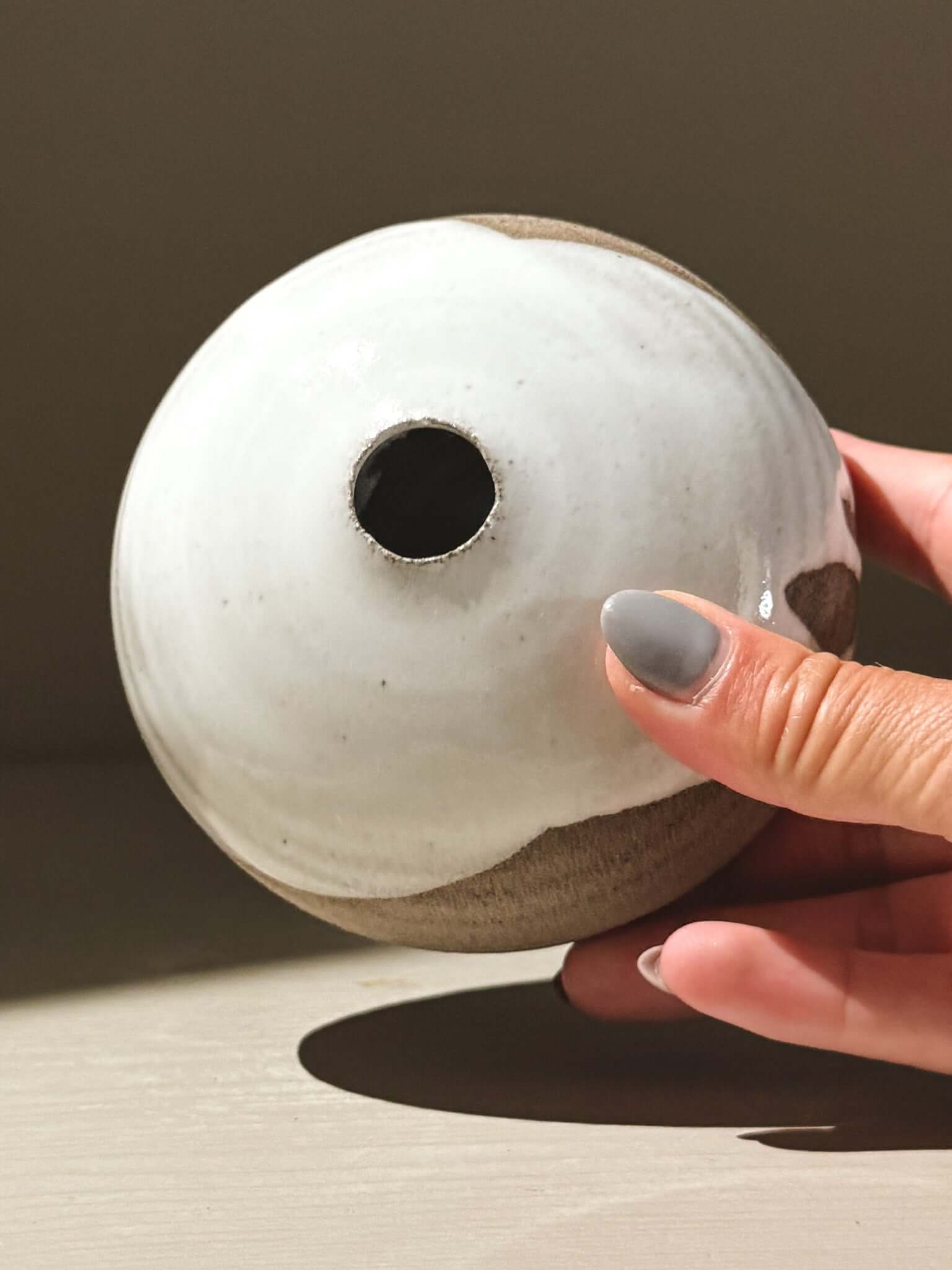 Hand holding a ceramic Orb Vase – Yuki Ash #11, showcasing its unique glaze and round shape.
