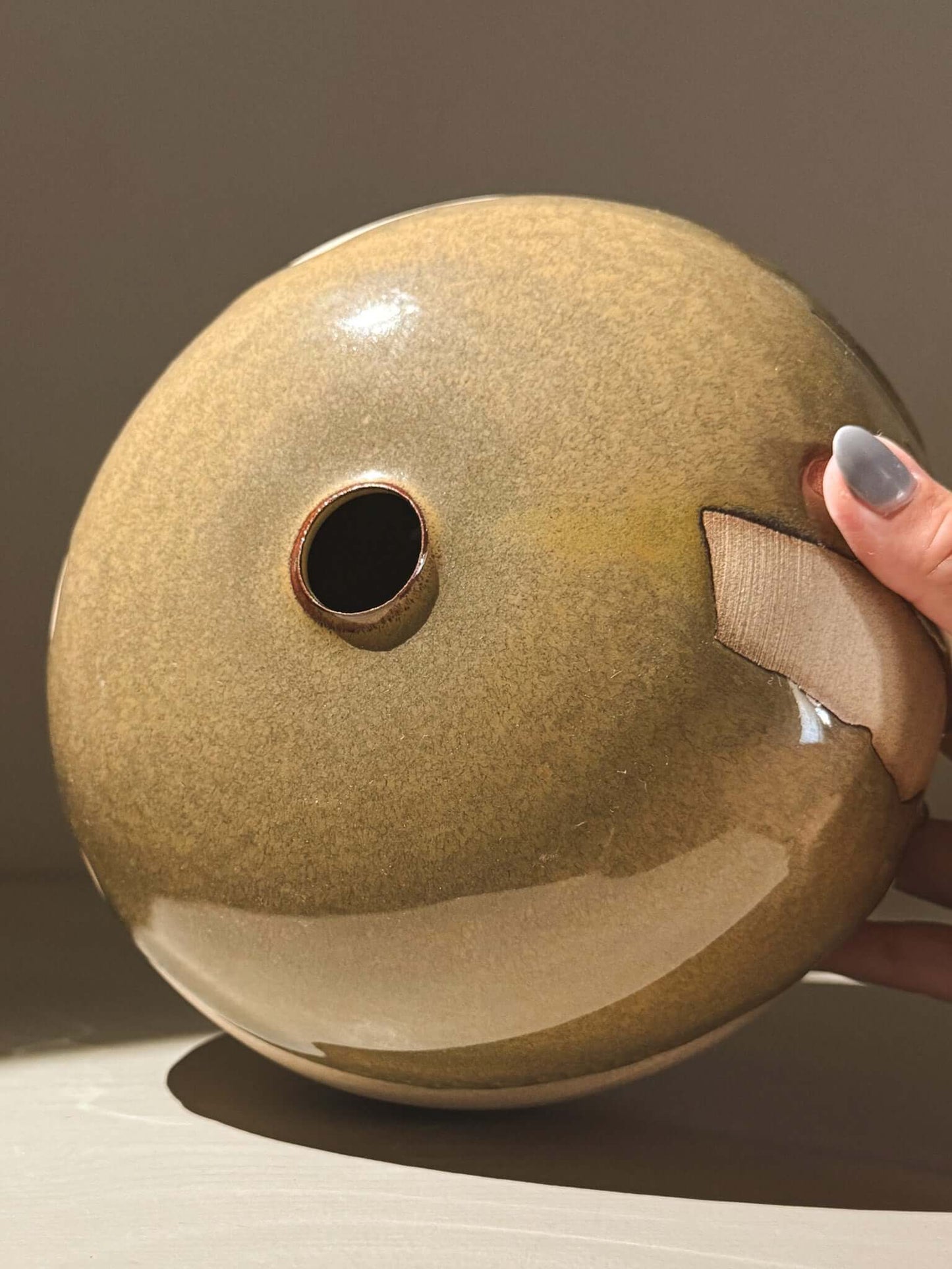 Hand holding a handmade ceramic Japanese orb vase, Orb Vase – Tenmoku #02, showcasing its unique glaze pattern.
