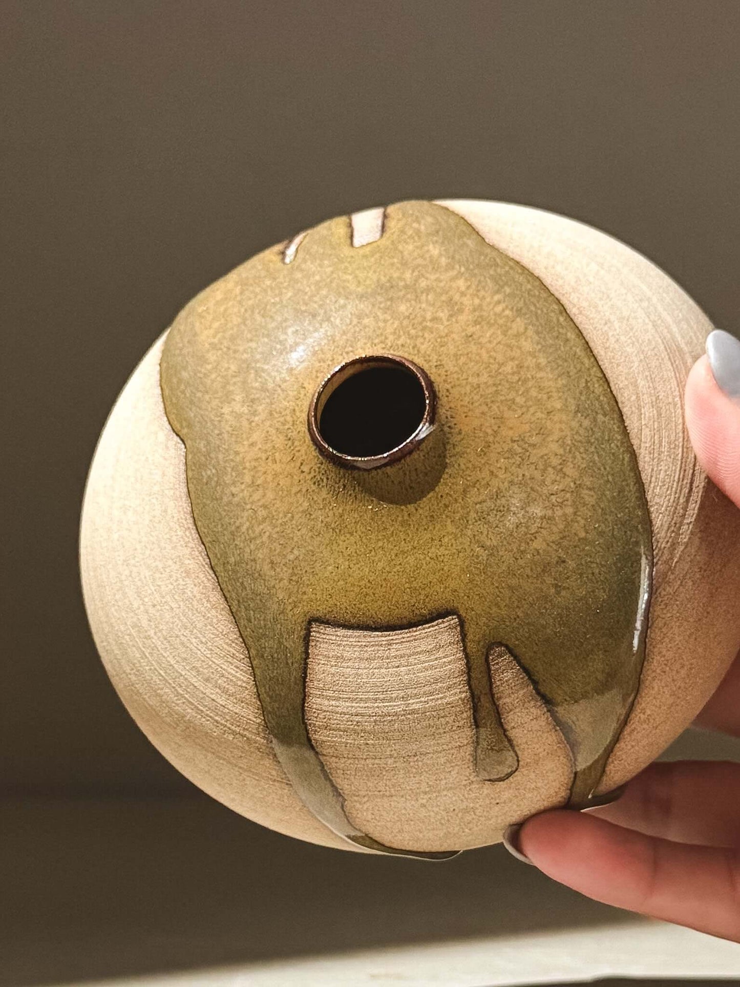 Hand holding an Orb Vase – Tenmoku #04, a handmade ceramic Japanese orb vase with a unique glaze pattern.