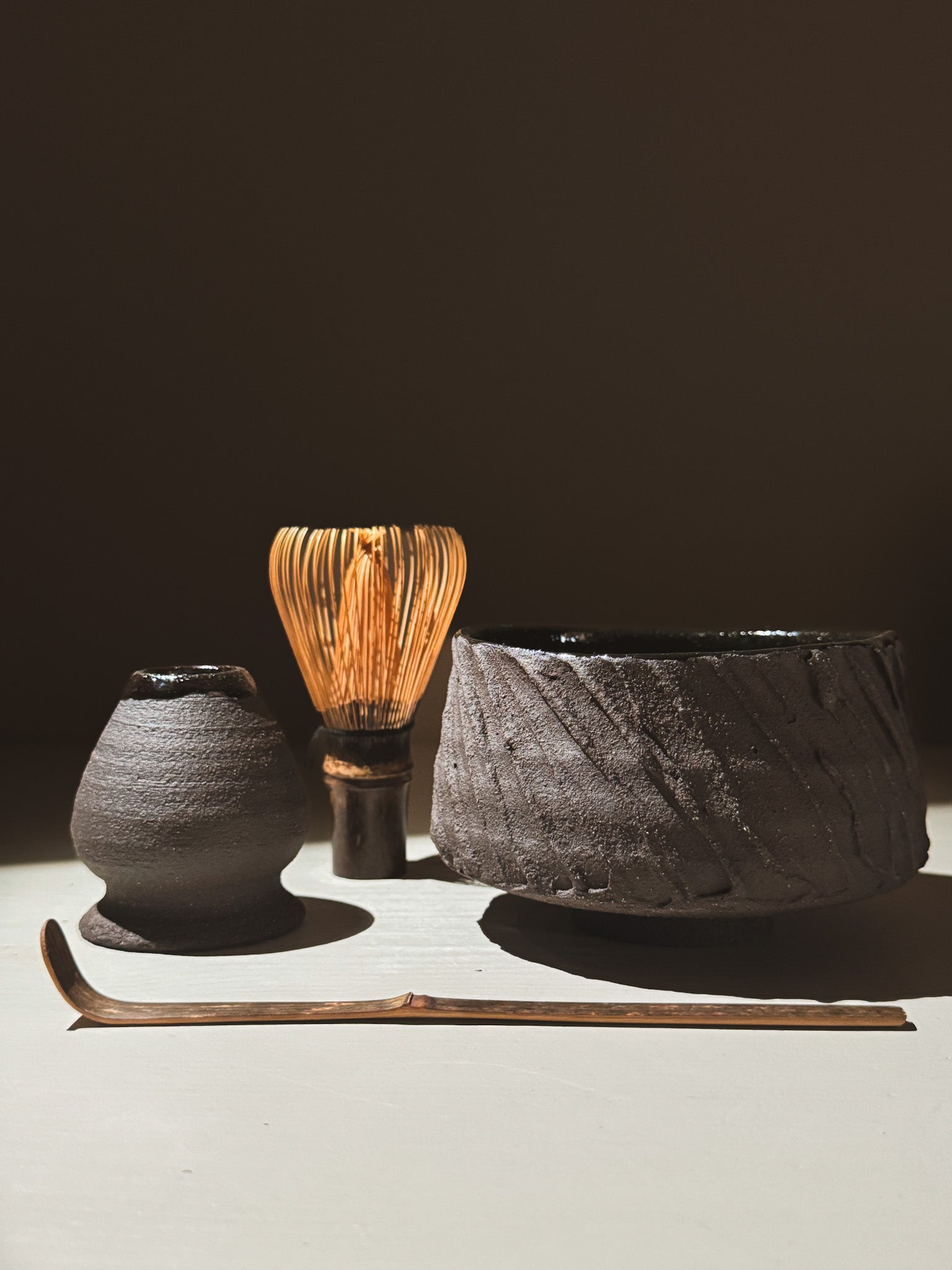 Kuro Matcha Bowl #01 alongside matcha whisk, scoop, and teapot made from dark earthy materials.