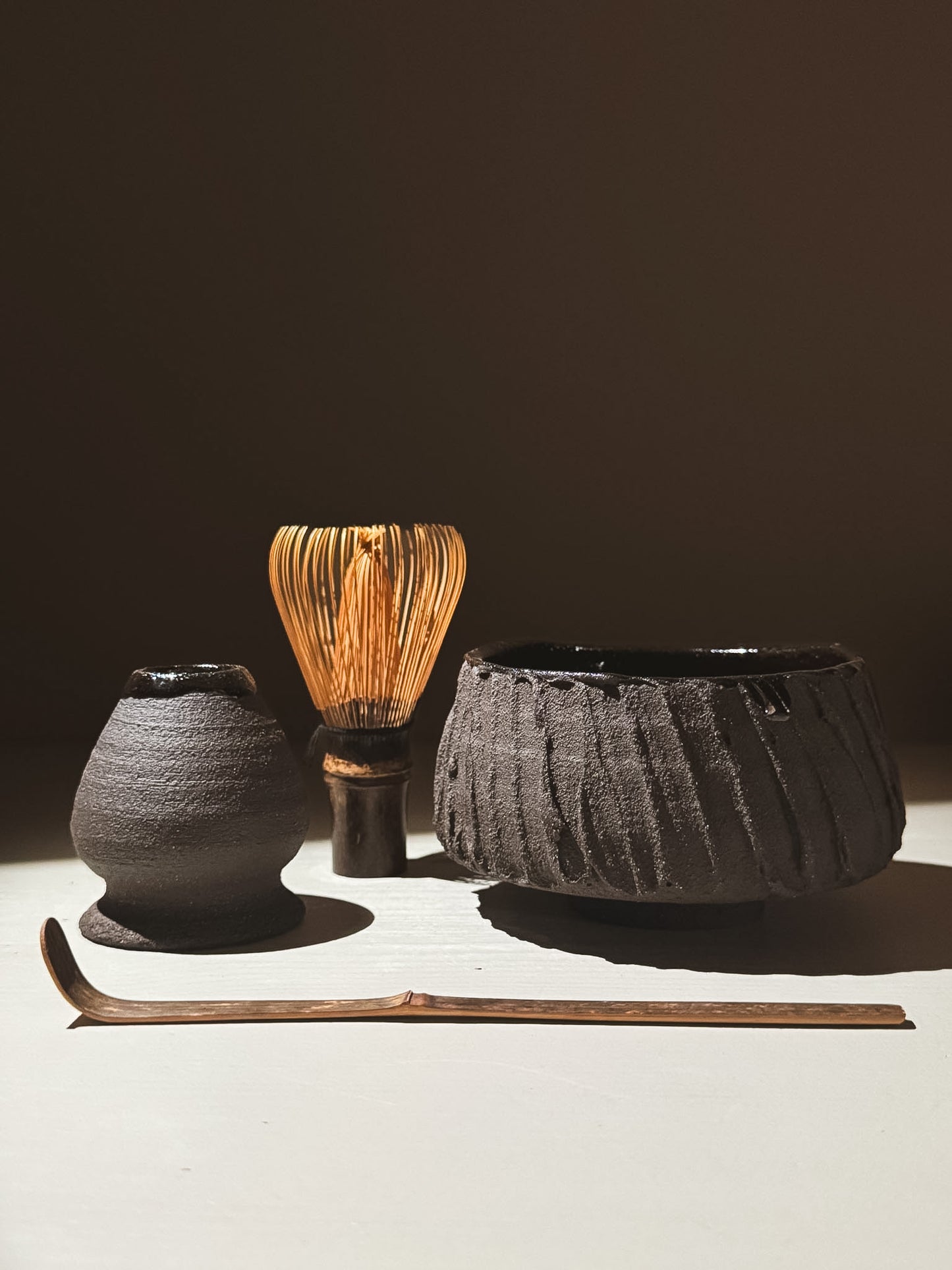 Kuro Matcha Bowl #02 alongside a traditional matcha whisk and scoop on a neutral background.