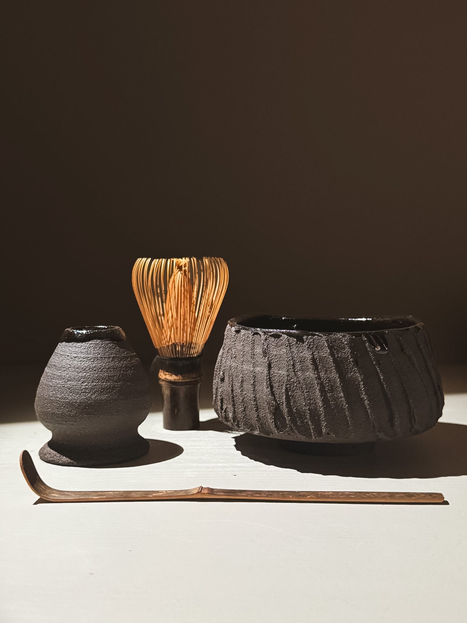 Kuro Matcha Bowl #02 alongside a traditional matcha whisk and scoop on a neutral background.