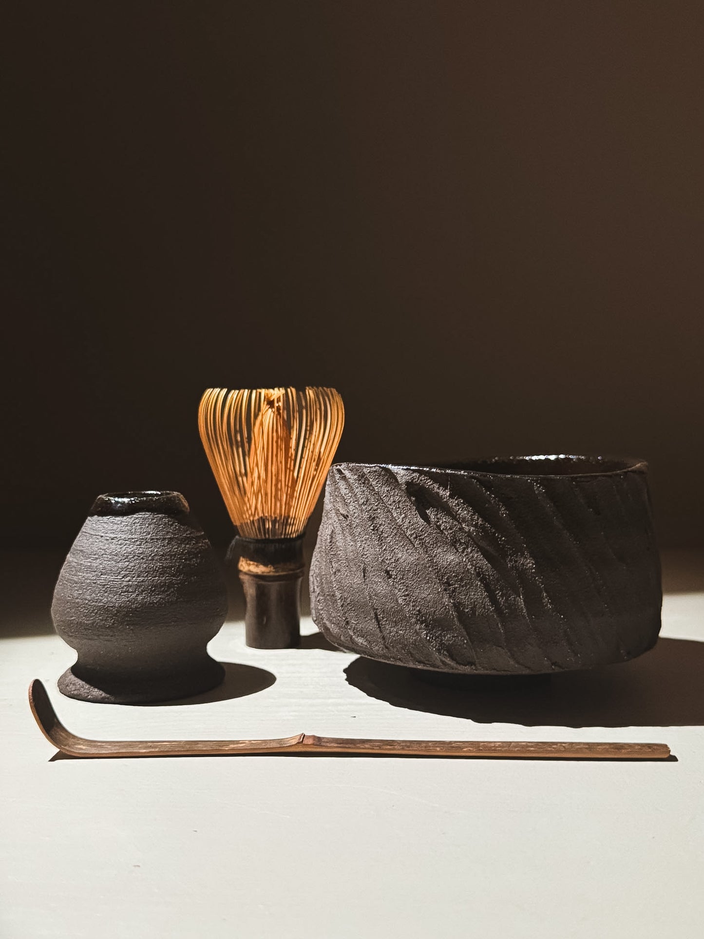 Kuro Matcha Bowl #04 alongside traditional matcha whisk, scoop, and dish, showcasing earthy textures and glossy finishes.