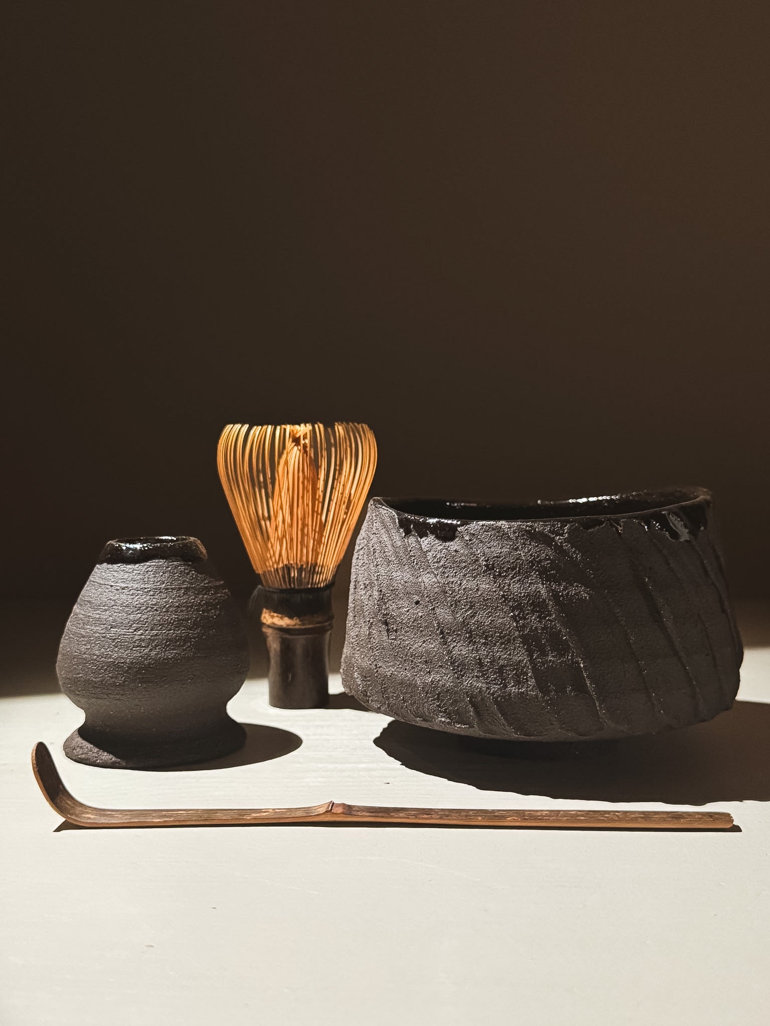 Kuro Matcha Bowl #05 with matcha whisk and accessory set on a neutral background, showcasing earthy textures and dark tones.